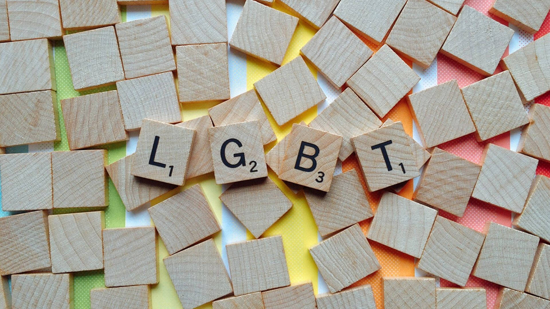 Subtle Lgbt 桌布 壁紙 — 木製 Scrabble 字母拼出 LGBT，排列在彩色條紋背景上。