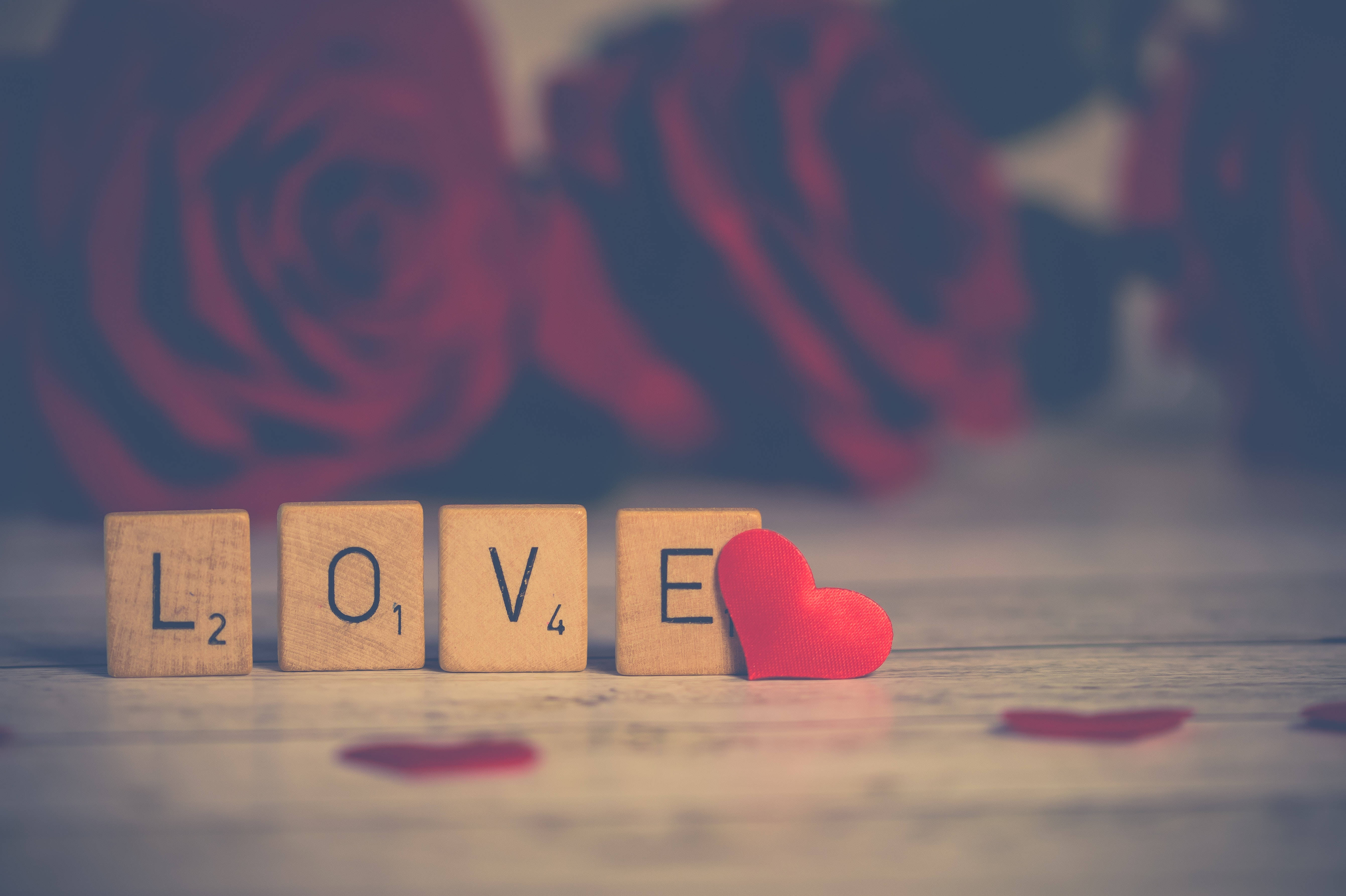 Romantic Love 桌布 壁紙 — 木製 Scrabble 字母拼出 LOVE，旁邊有一個紅心，背景是模糊的紅玫瑰。