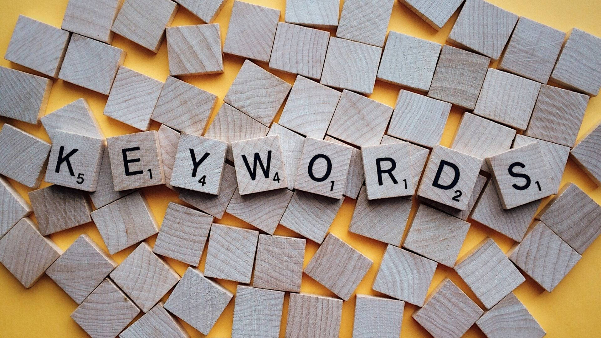 木紋 桌布 壁紙 — 木製 Scrabble 字母牌在鮮黃色背景上拼出「KEYWORDS」，並散落著其他字母牌。
