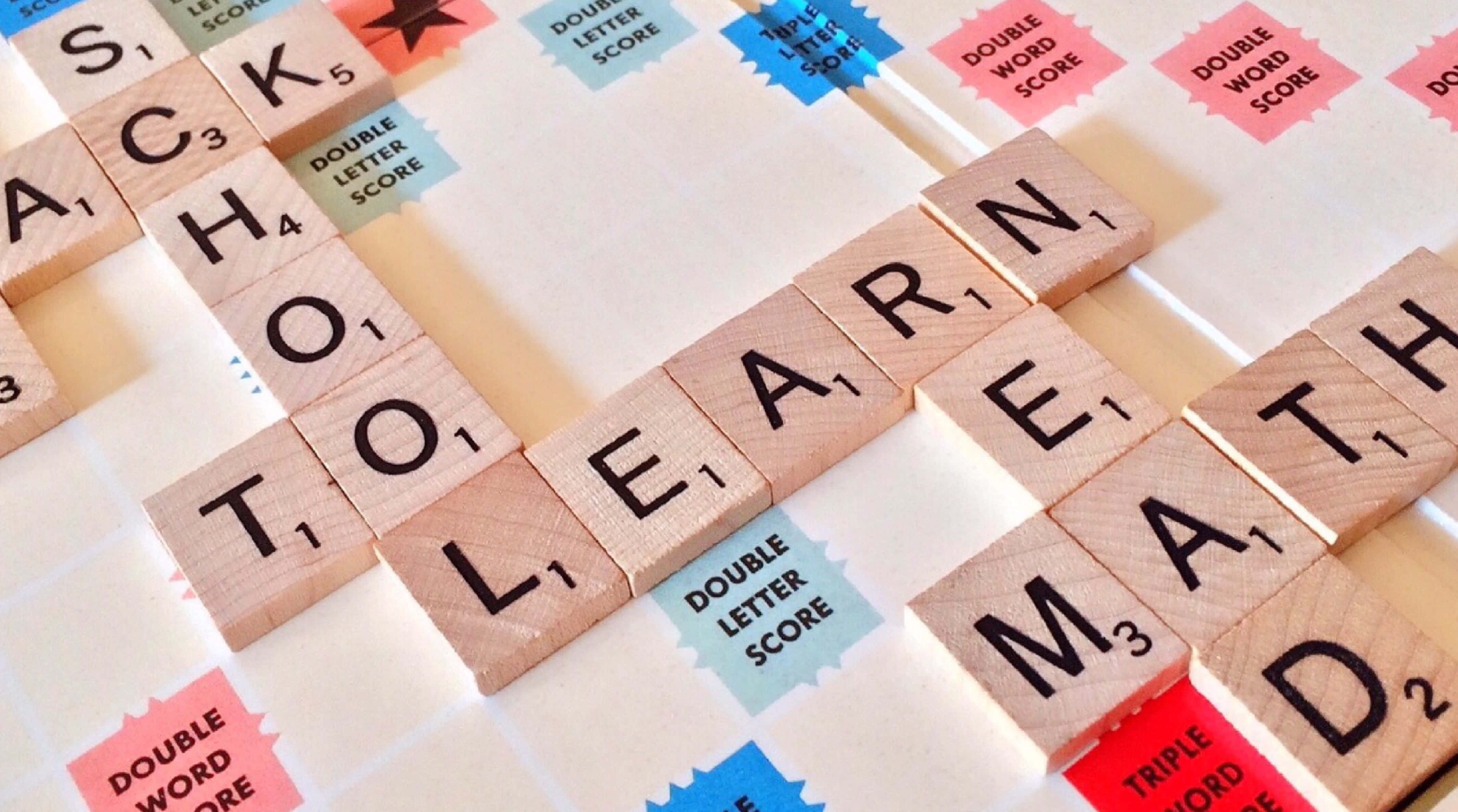 Educational Games 桌布 壁紙 — 木製 Scrabble 字母牌在色彩繽紛的遊戲板上拼出「SCHOOL TO LEARN MATH」，並帶有獎勵格。
