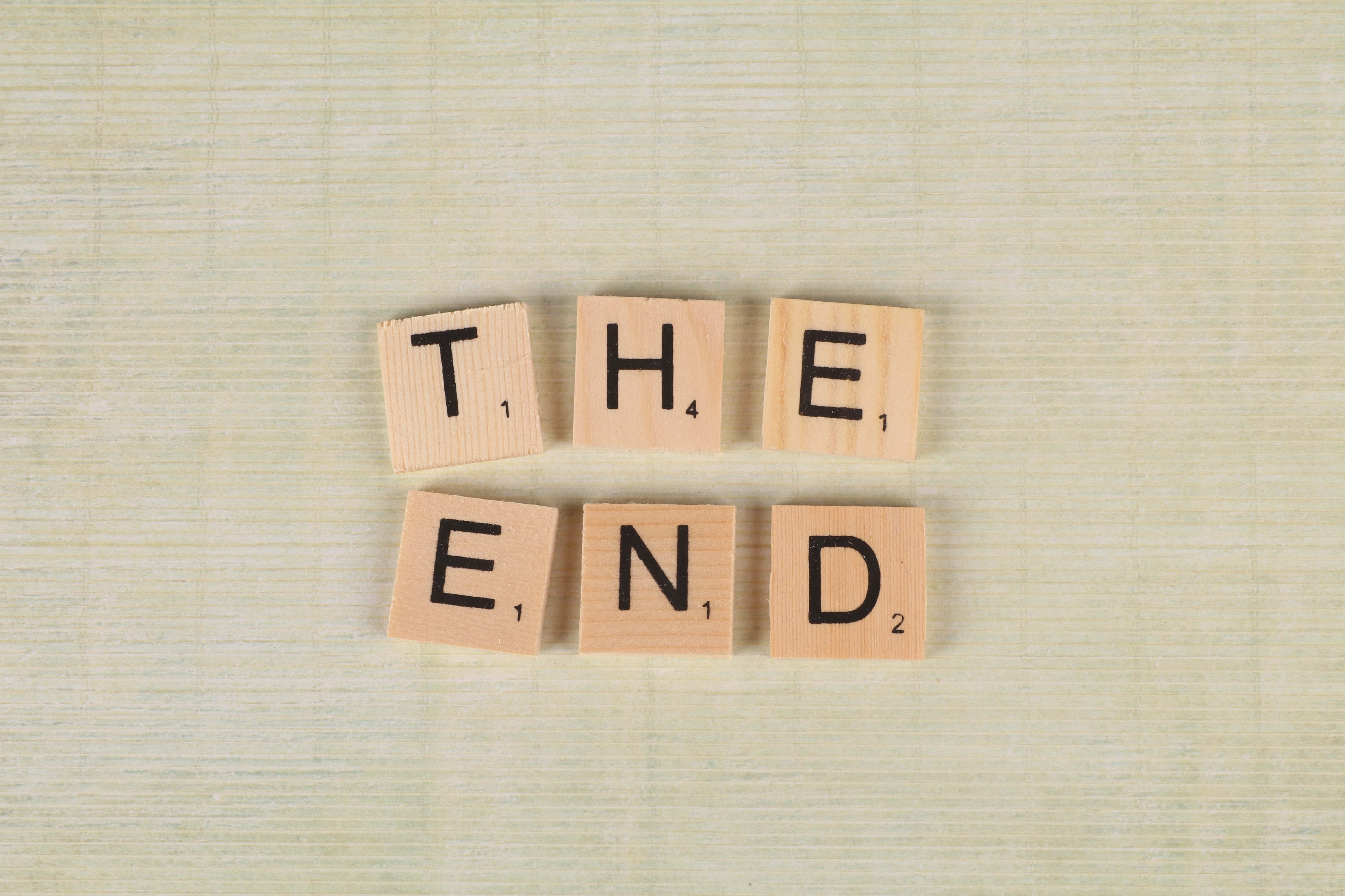 the end 桌布 壁紙 — 木製 Scrabble 字母牌拼出 'THE END'，放在有紋理的米色表面上。