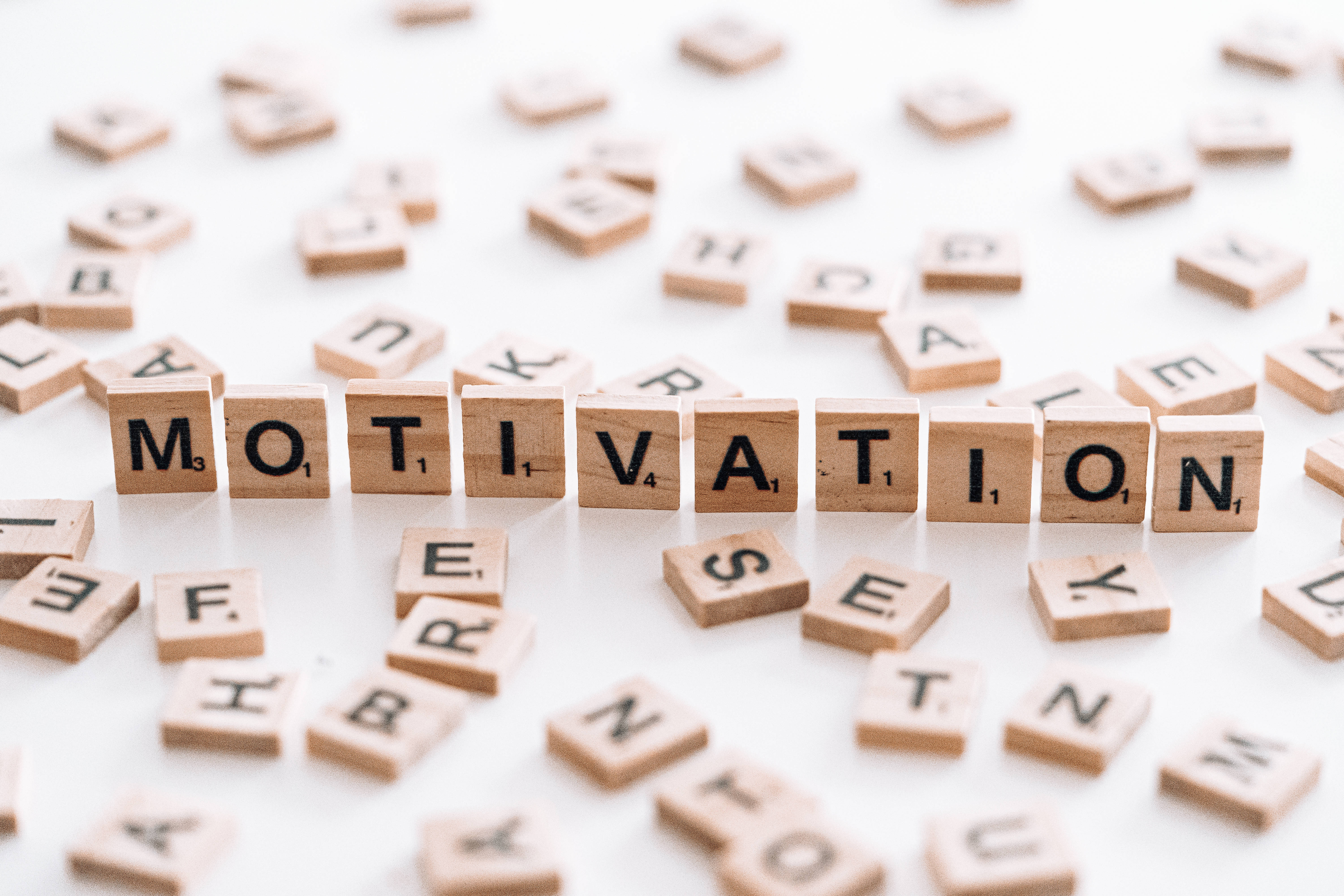 Motivation 桌布 壁紙 — 木製 Scrabble 字母磚在明亮的白色背景上拼出動力，周圍散落著字母。