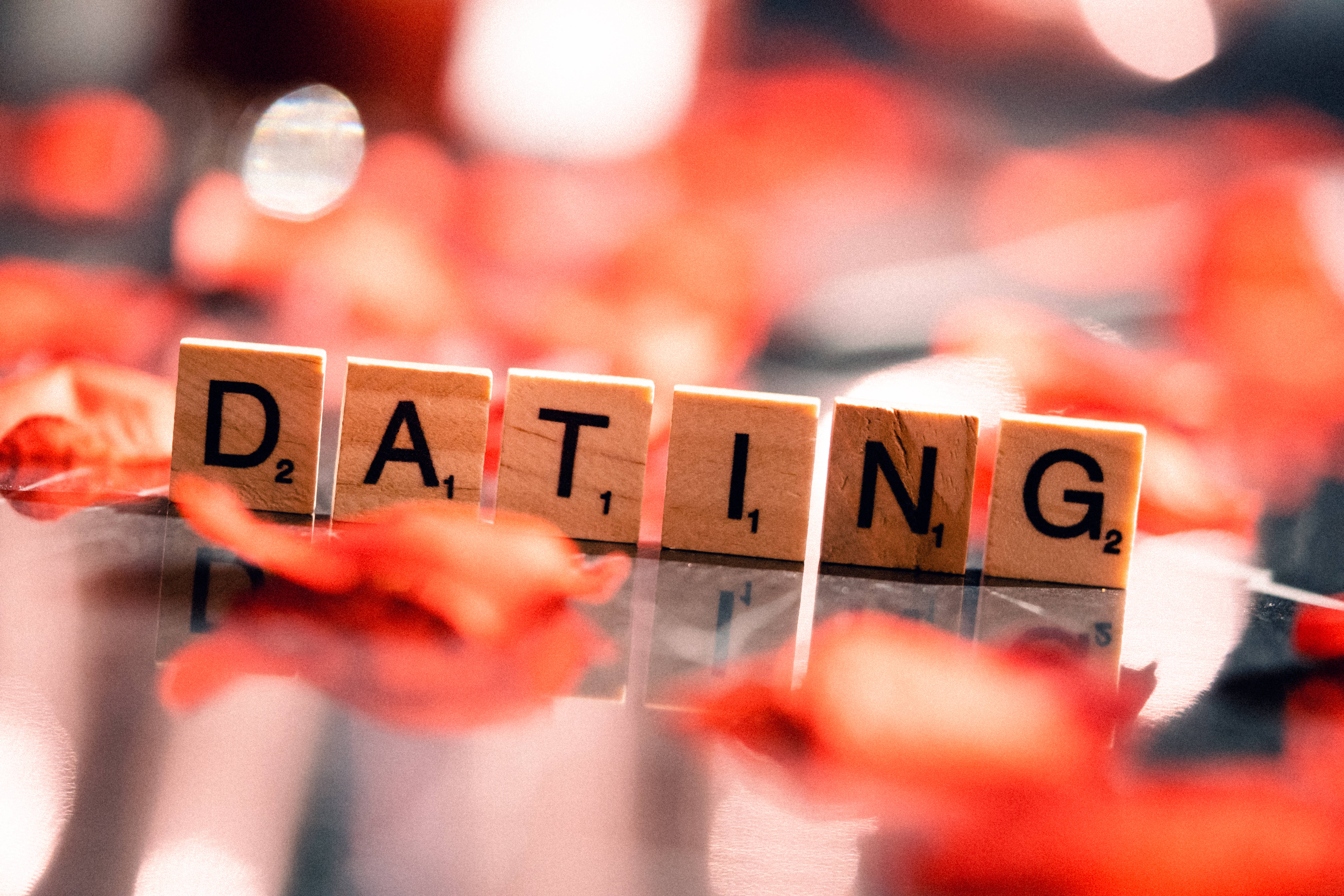 愛情桌面 桌布 壁紙 — 木製 Scrabble 拼字塊拼出 dating，放在光滑表面上，周圍散落著紅色玫瑰花瓣。
