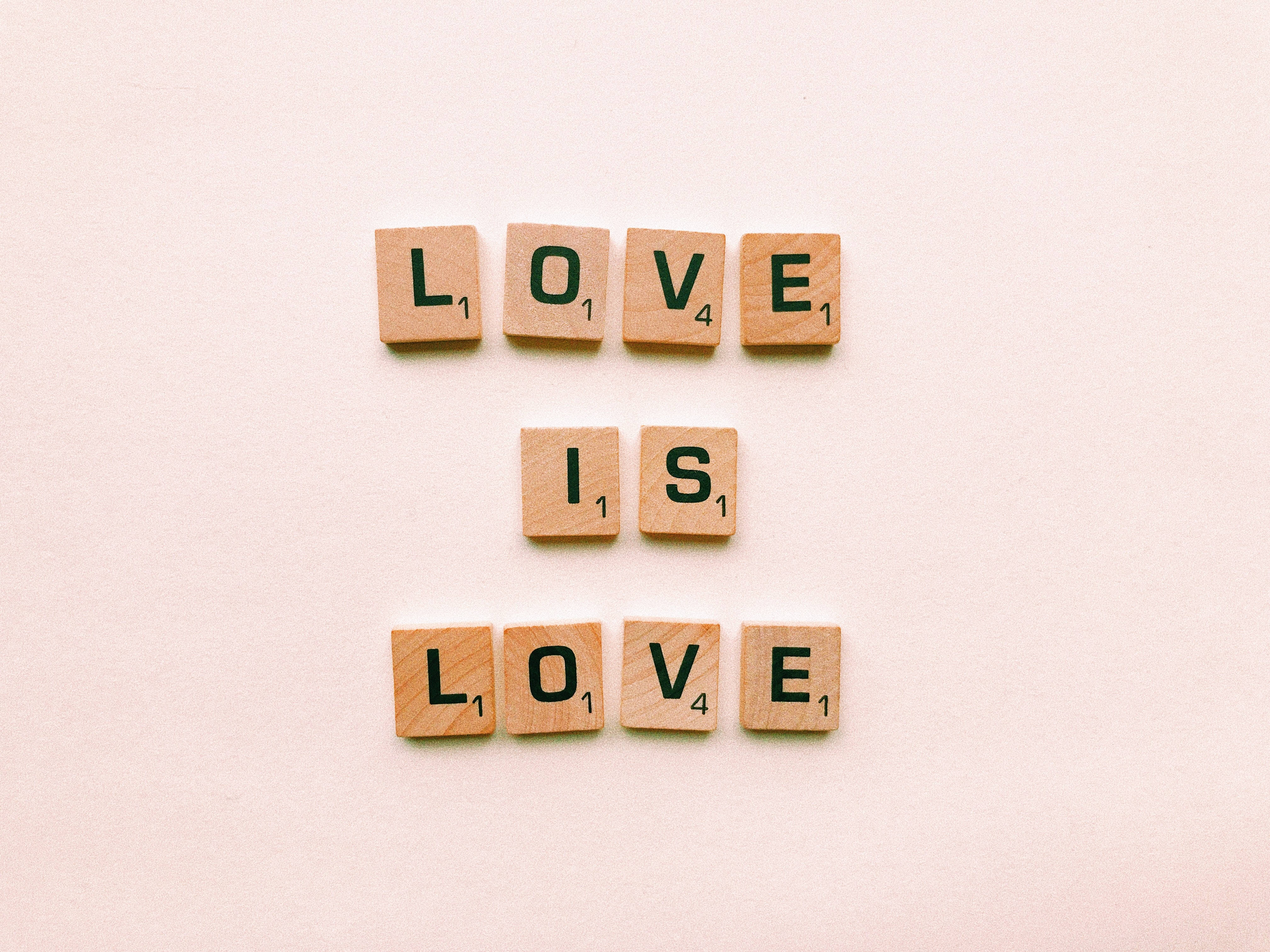 Romantic Love 桌布 壁紙 — 木製Scrabble字母牌在柔軟的米色背景上以極簡排列拼出「LOVE IS LOVE」。