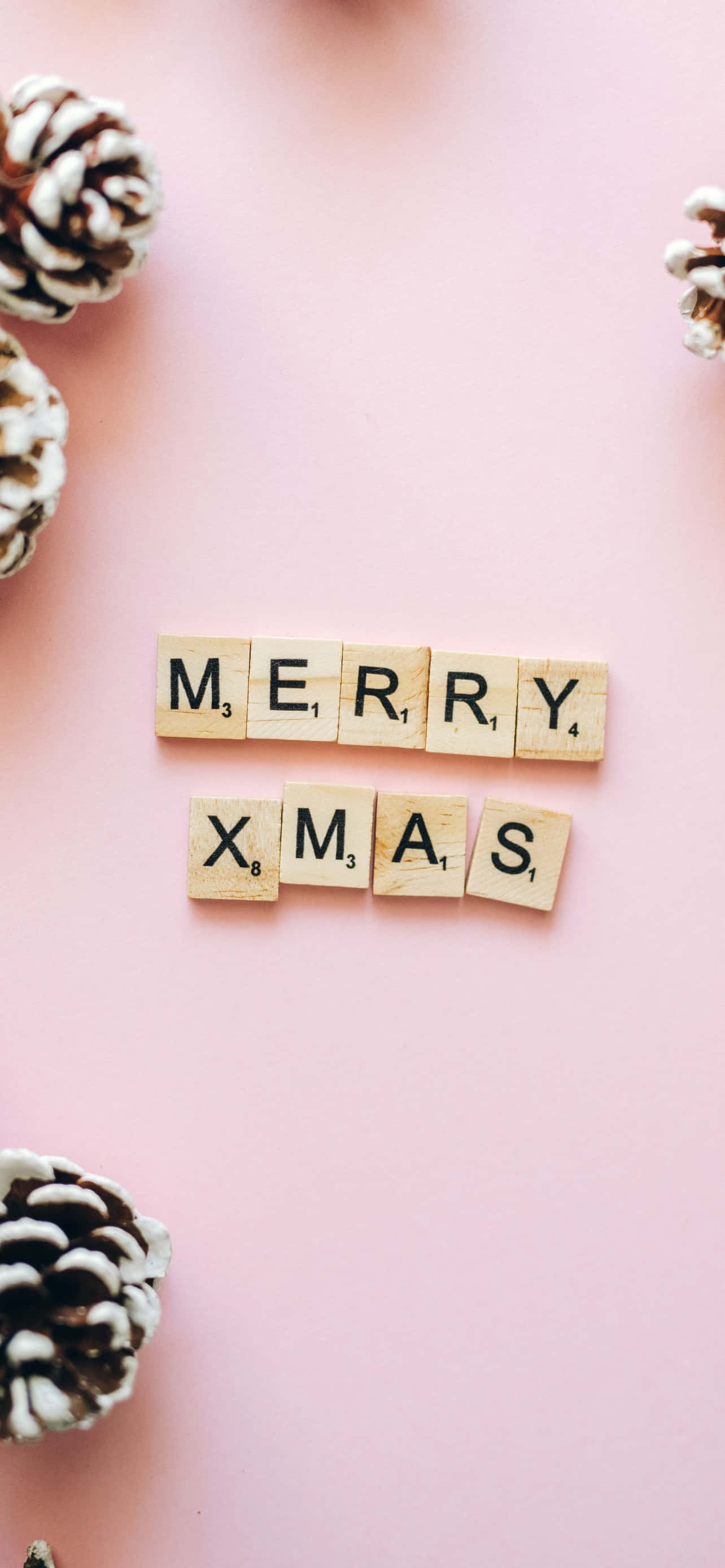 聖誕節 桌布 壁紙 — 木製Scrabble字母牌在柔軟的粉紅色背景上拼出merry xmas，周圍環繞著松果。