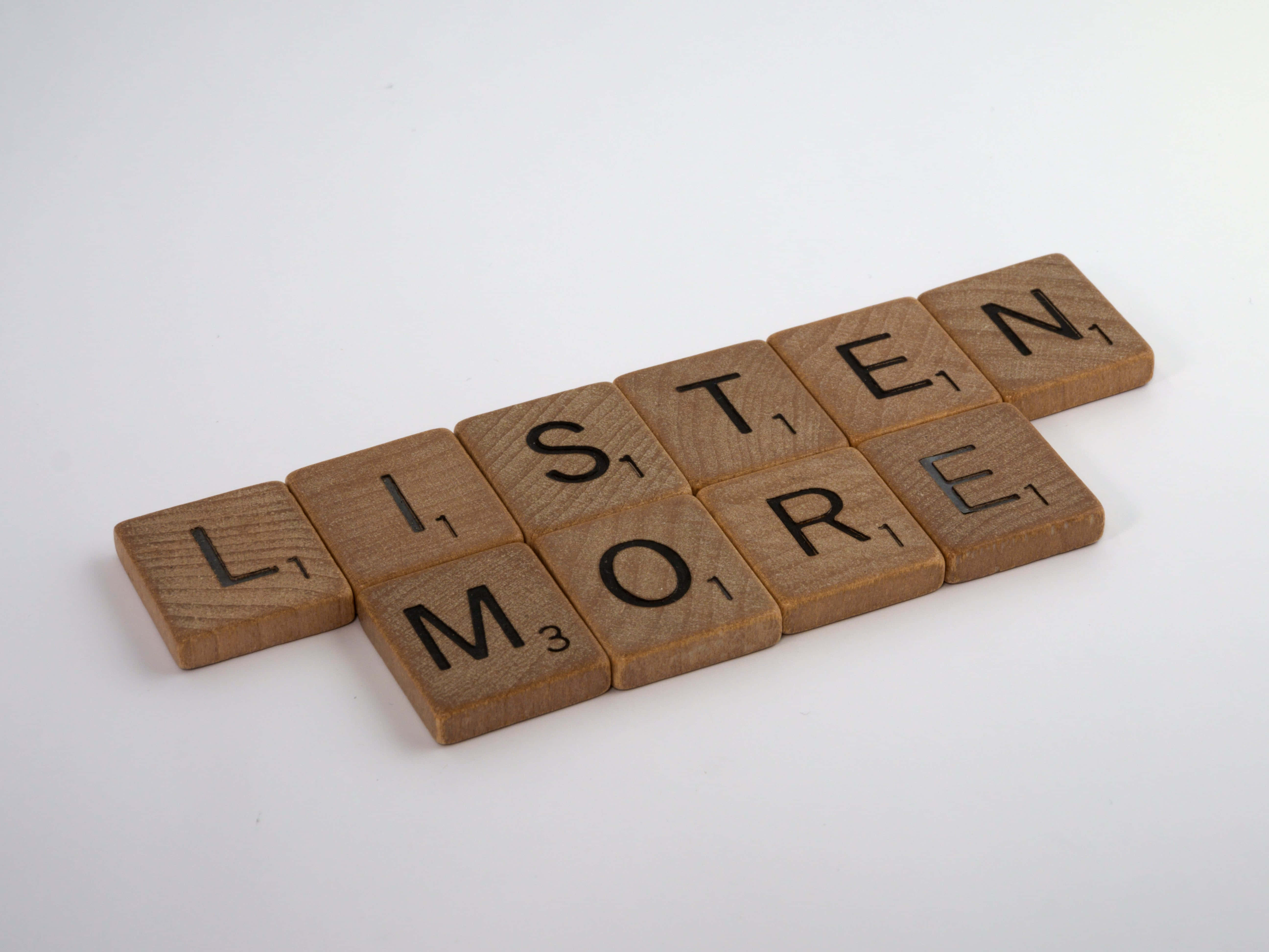 木紋 桌布 壁紙 — 木製Scrabble字母磚拼出「LISTEN MORE」，以對角線排列在純白背景上。