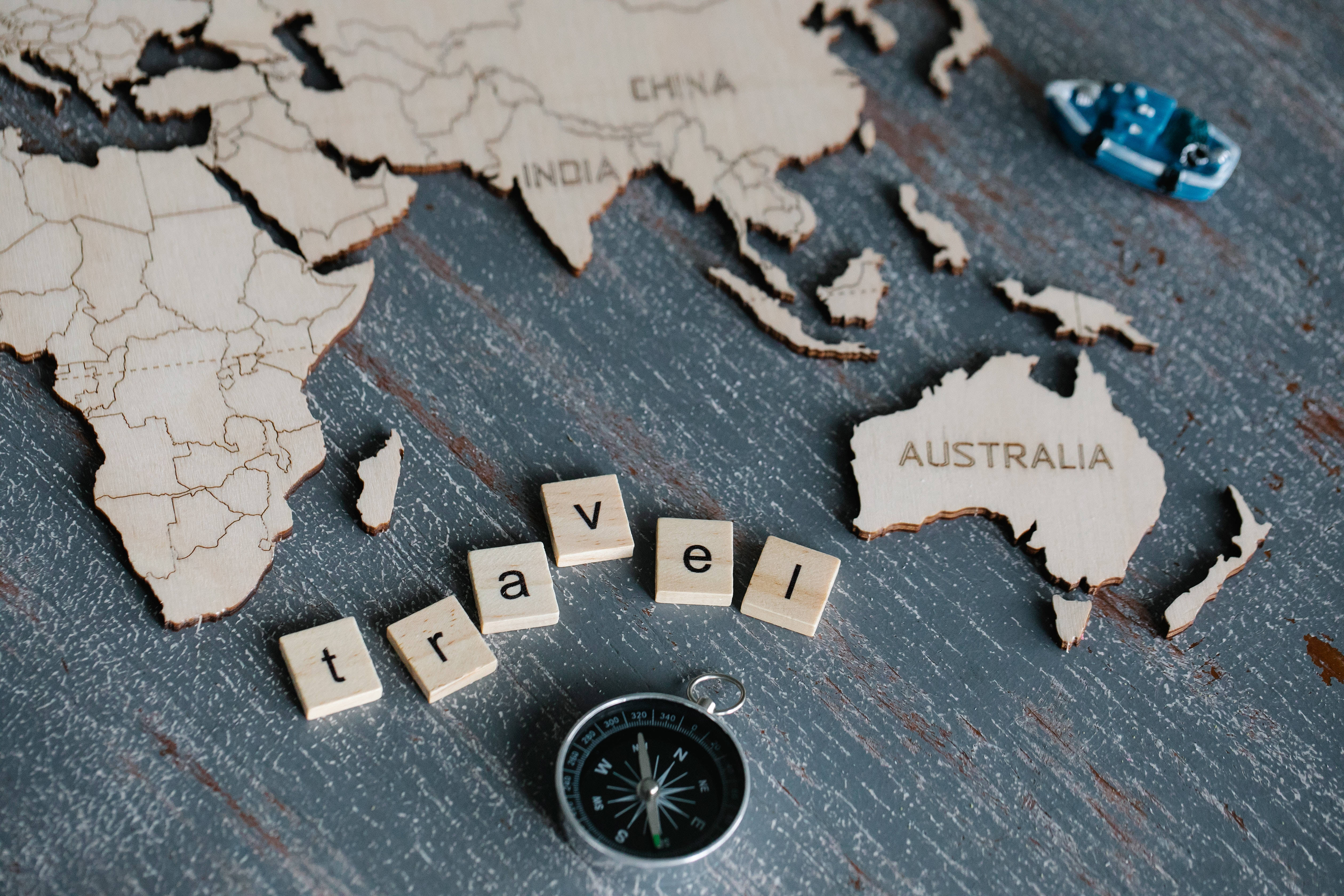 Map 桌布 壁紙 — 木製世界地圖拼圖和 Scrabble 字母磚拼出 travel，連同指南針在帶有紋理的灰色表面上。