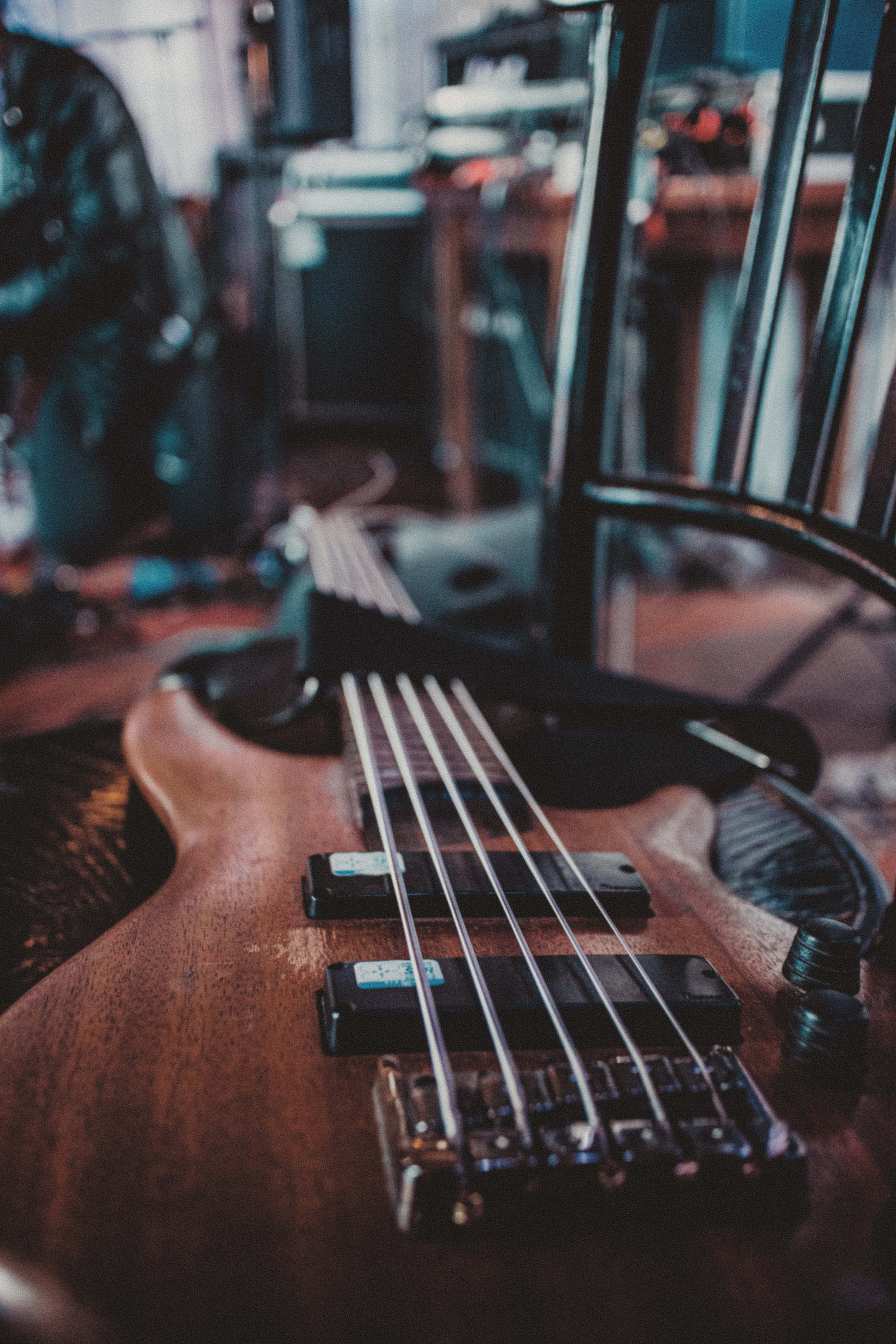 Bass Guitar 桌布 壁紙 — 木製低音吉他特寫，擱在昏暗音樂室的椅子上，背景有模糊的設備。