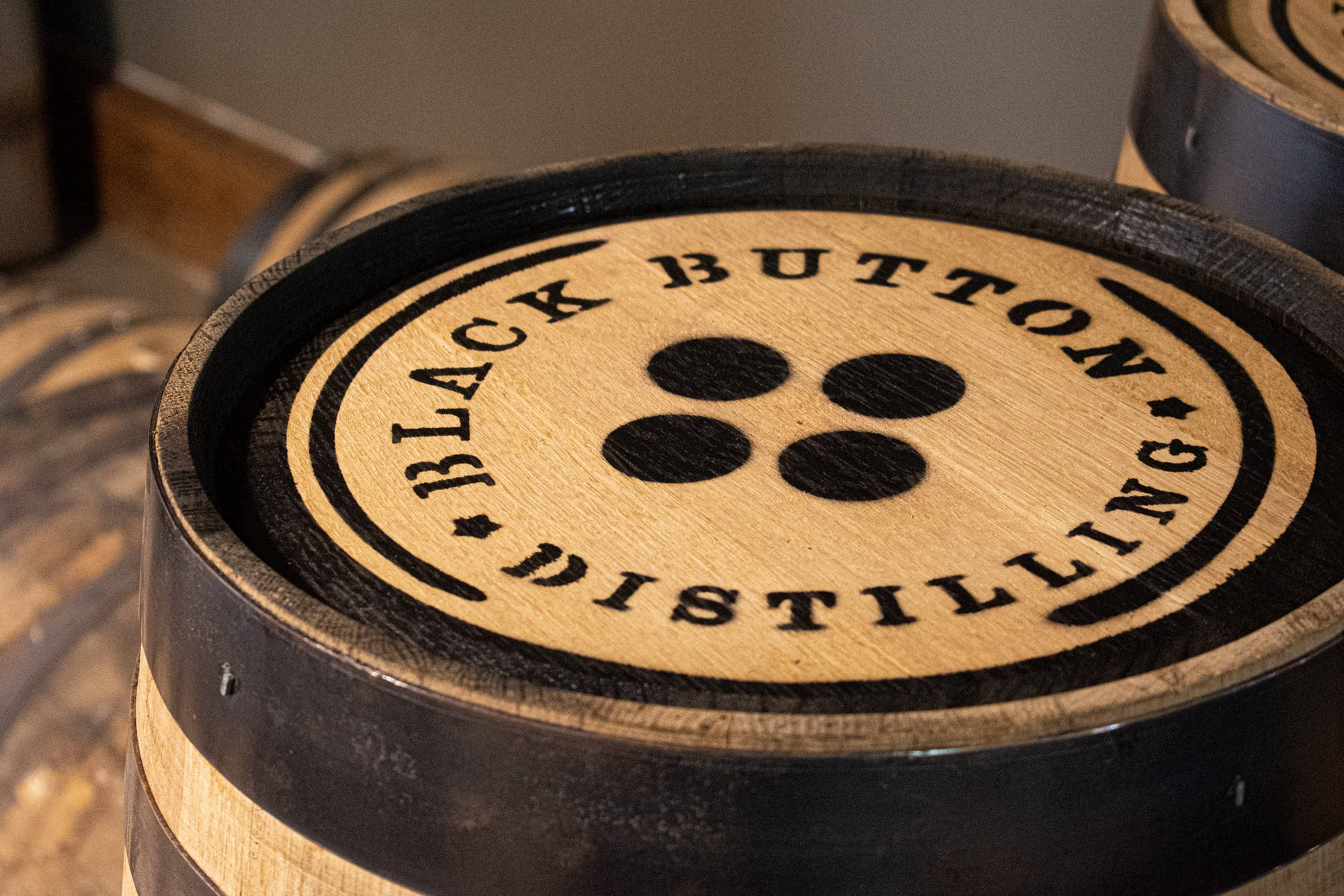 木紋 桌布 壁紙 — 木製威士忌酒桶的特寫，桶板上印有 'Black Button Distilling' 標誌和四個黑點。