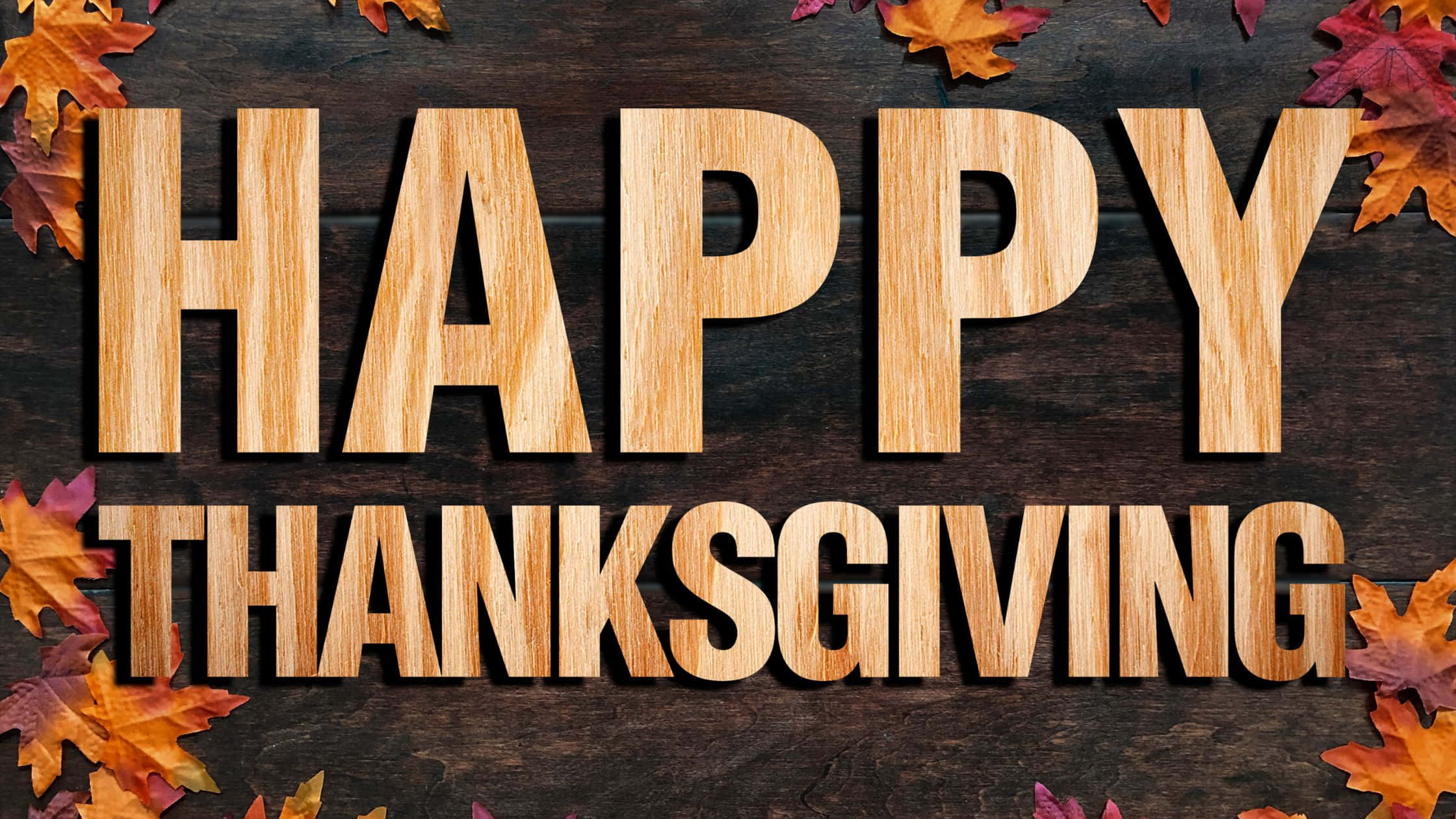Thanksgiving Desktop 桌布 壁紙 — 木製字母在深色木質表面上拼出 happy thanksgiving，周圍環繞著秋葉。