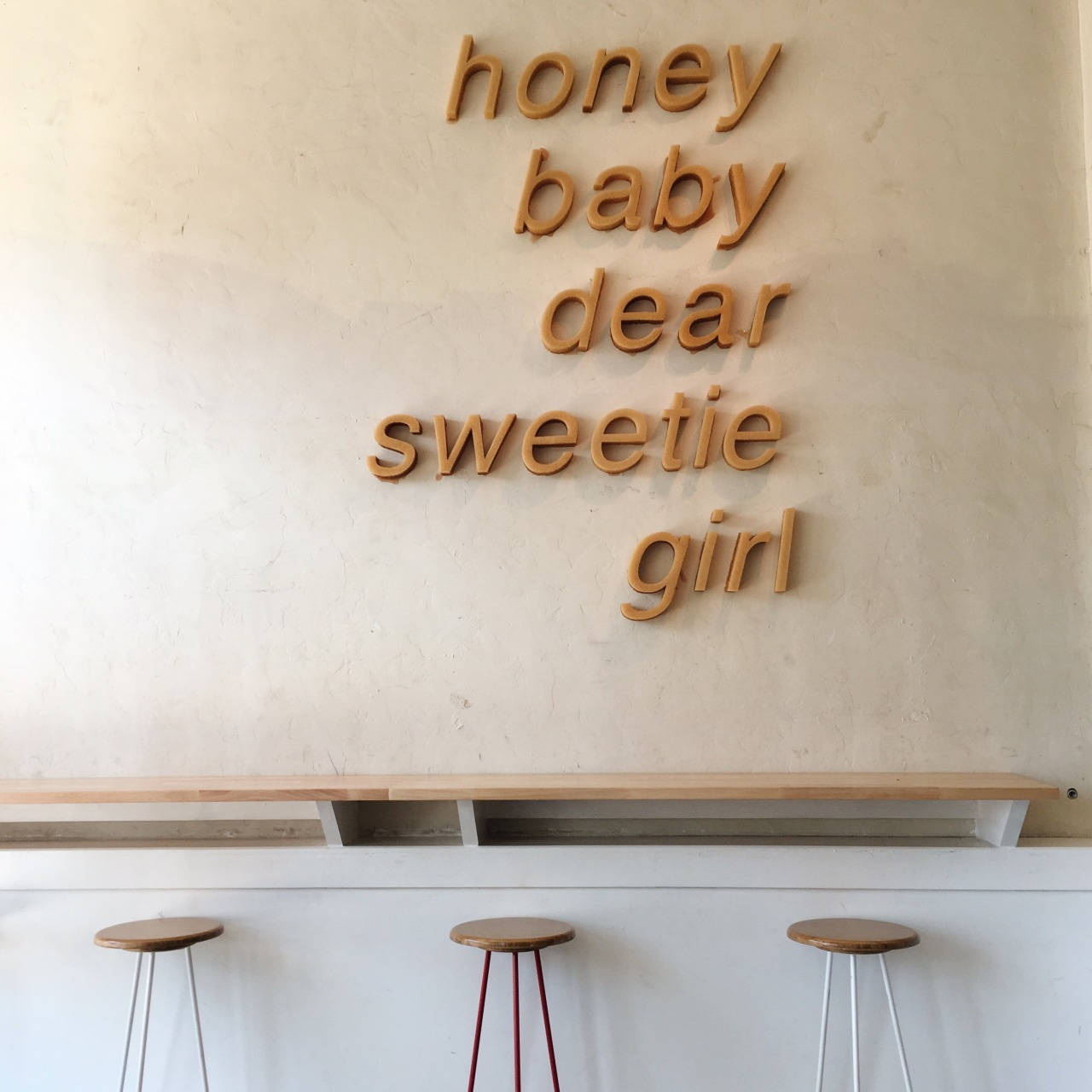米色風格 桌布 壁紙 — 木製字母拼出 honey baby dear sweetie girl，安裝在紋理米色牆上，下方是簡約凳子。