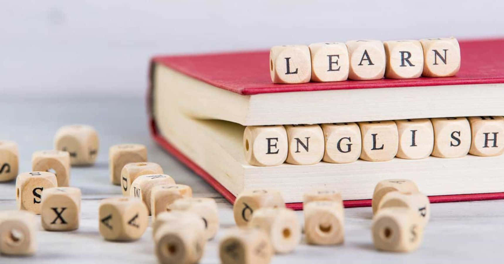 English 桌布 壁紙 — 木製字母方塊在紅色書本上拼出「LEARN ENGLISH」，淺色木質表面上散落著方塊。