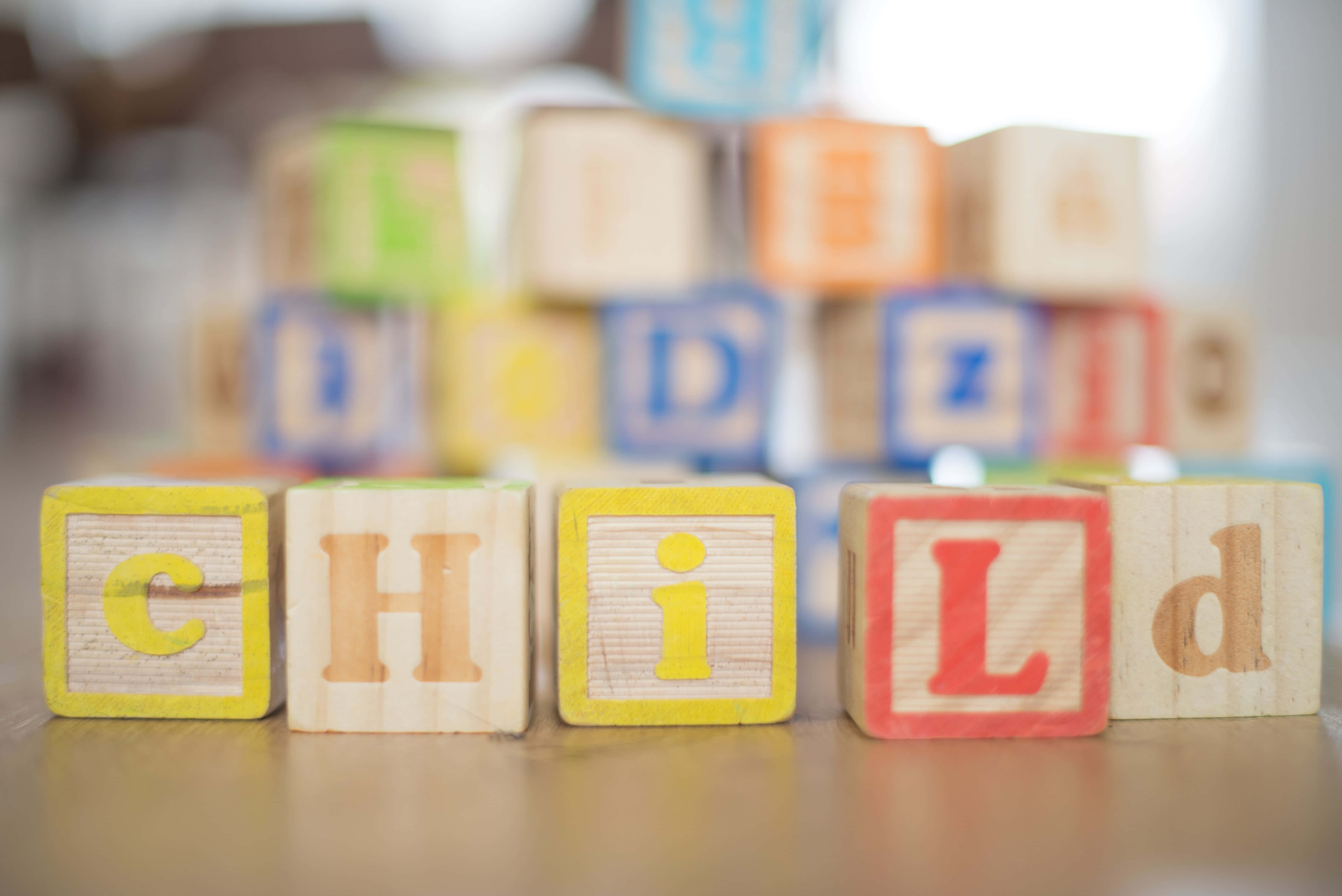Educational Games 桌布 壁紙 — 木製字母積木在前景拼出「CHILD」，後面有彩色積木堆疊在木質表面上。