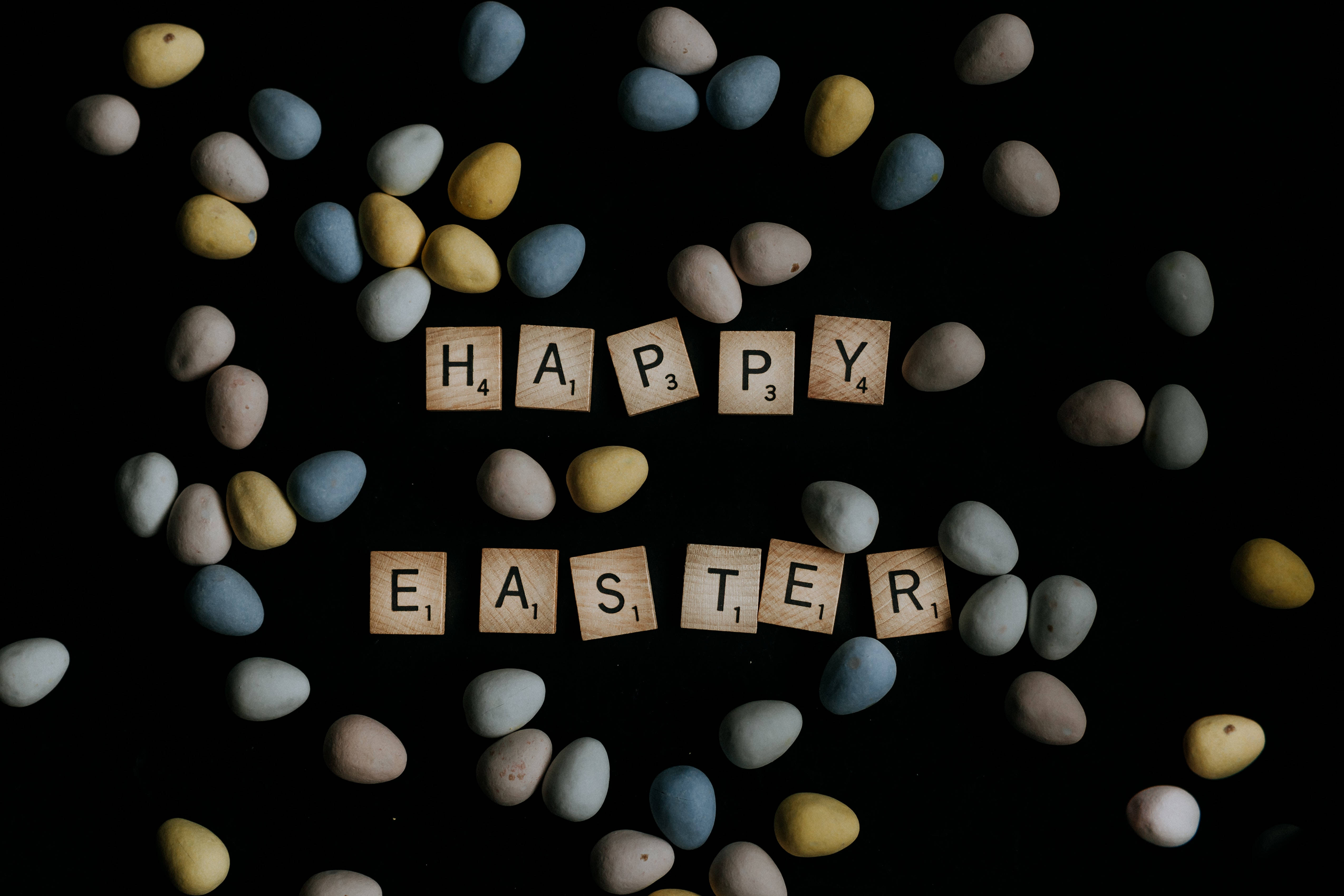 Happy Easter 桌布 壁紙 — 木製拼字磚在黑色背景上拼出happy easter，周圍環繞著粉彩蛋。