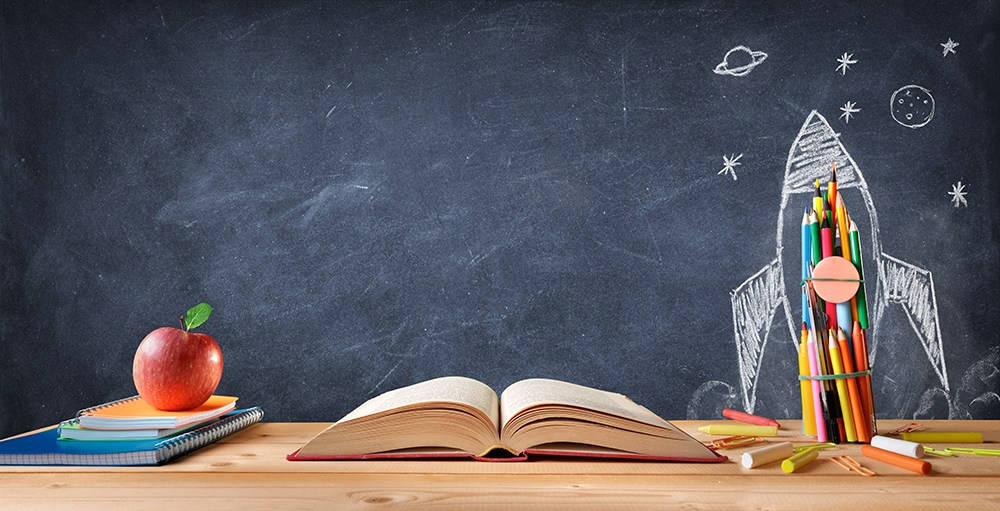 Education 桌布 壁紙 — 木製書桌上放著一本打開的書、紅蘋果和彩色鉛筆，旁邊黑板上有粉筆畫的火箭船。