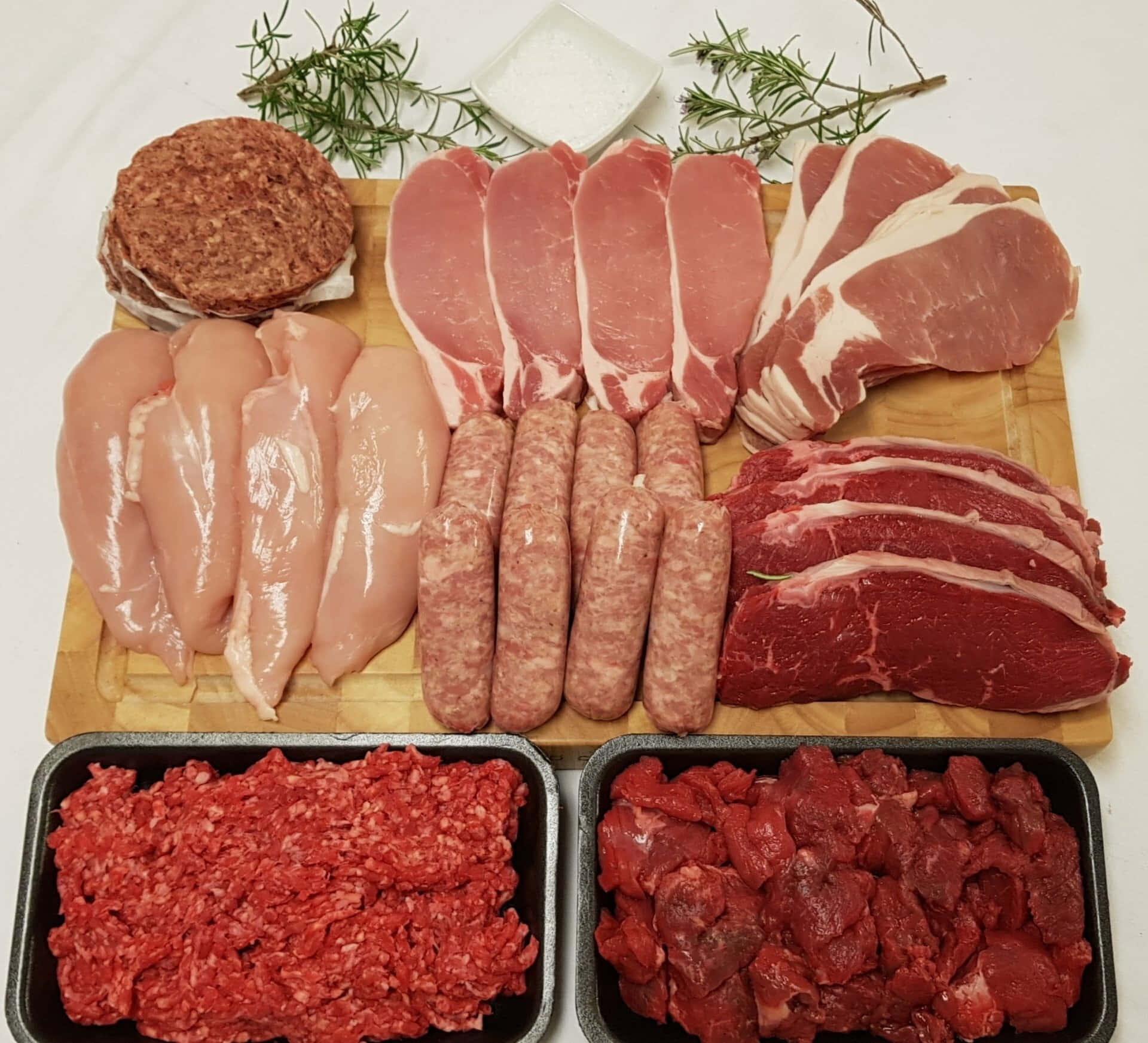 meat 桌布 壁紙 — 木製砧板上展示各種生肉，包括雞胸肉、豬排、牛排、香腸、牛絞肉和羊排，並以迷迭香和鹽裝飾。