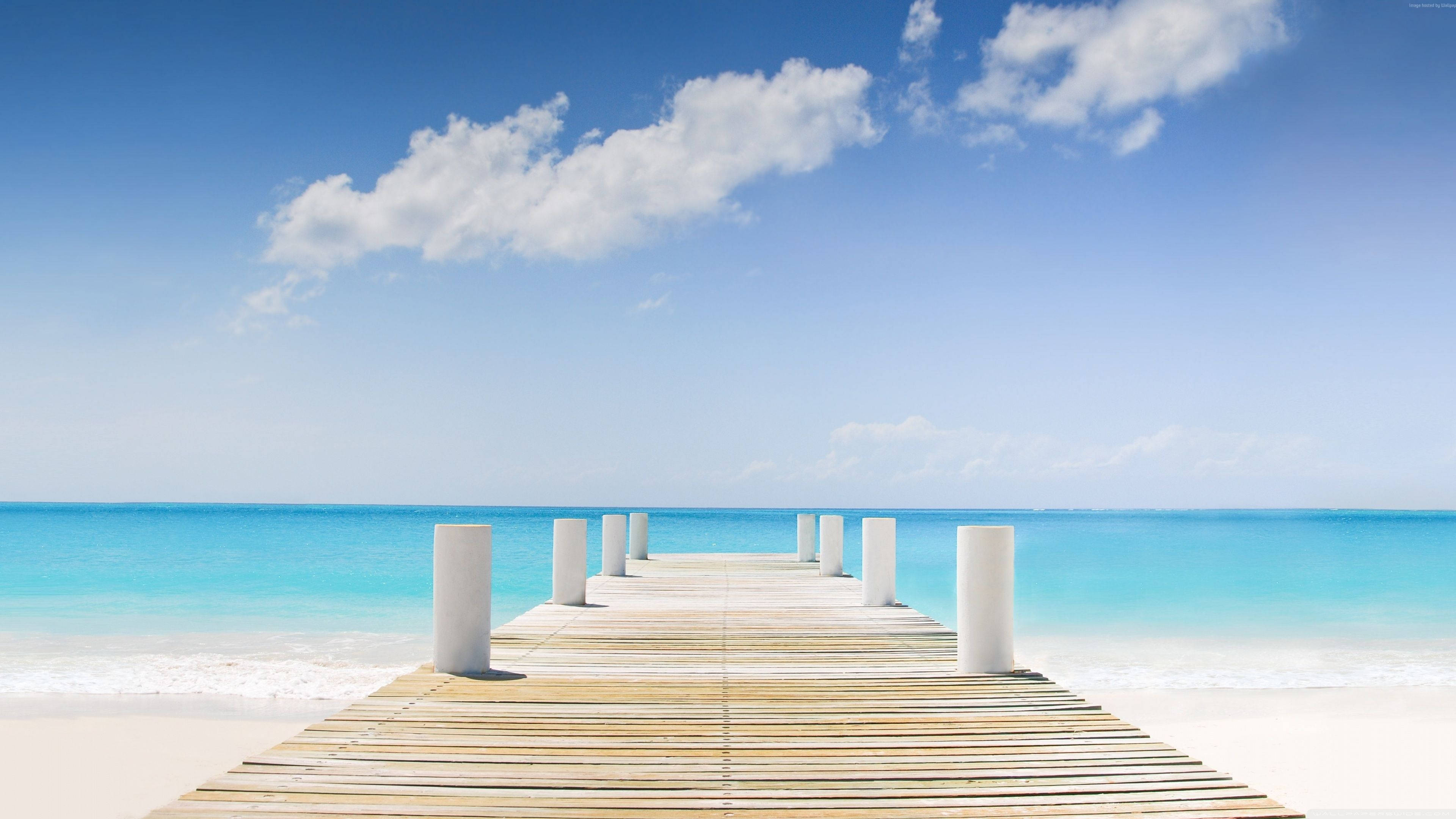 Turks And Caicos 桌布 壁紙 — 木製碼頭延伸至藍綠色海洋，上方是明亮的藍天和蓬鬆的白雲。