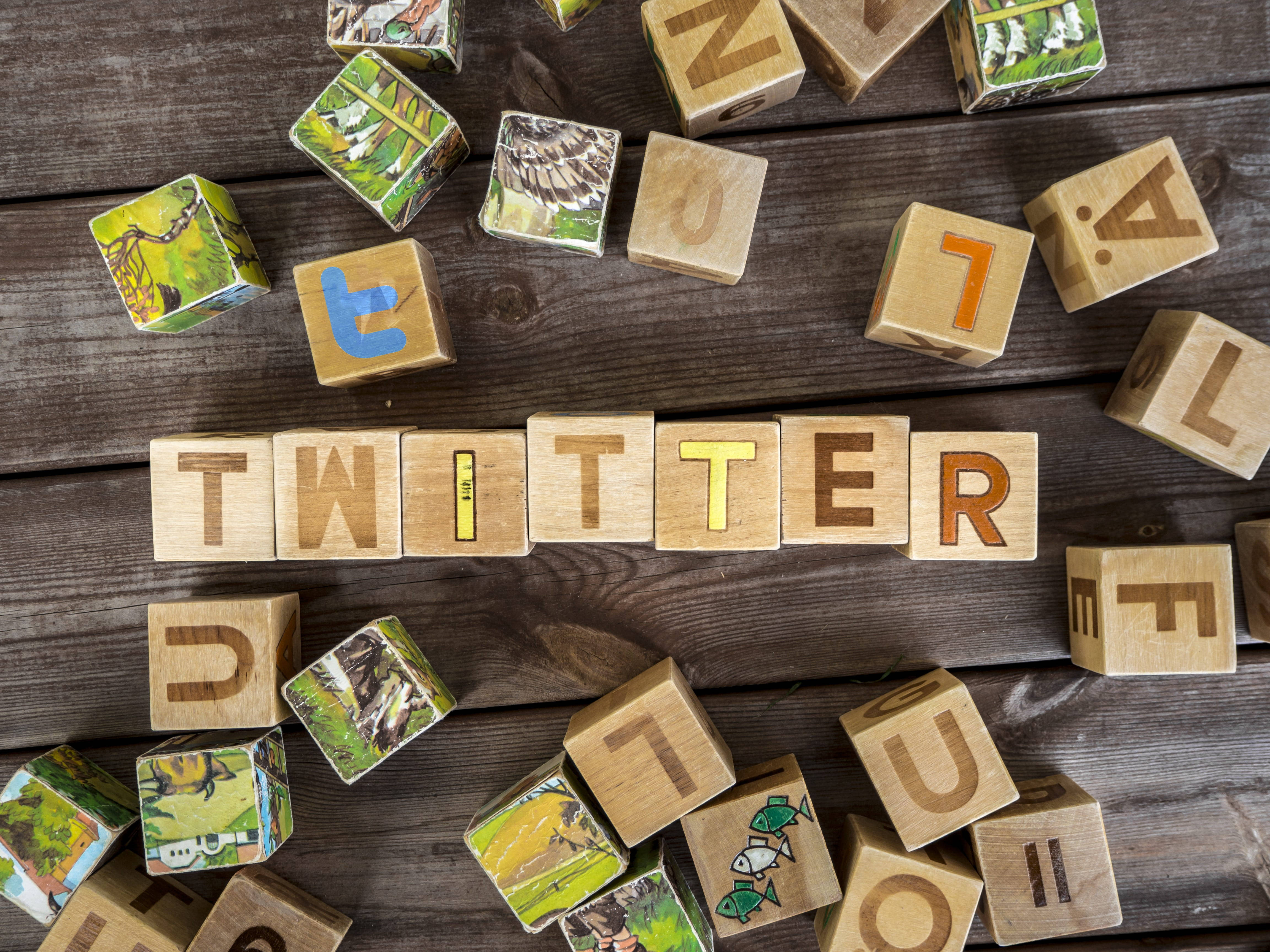 Twitter 桌布 壁紙 — 木製積木在深色鄉村風桌子上拼出 'TWITTER'，周圍散落著帶有自然場景的字母積木。