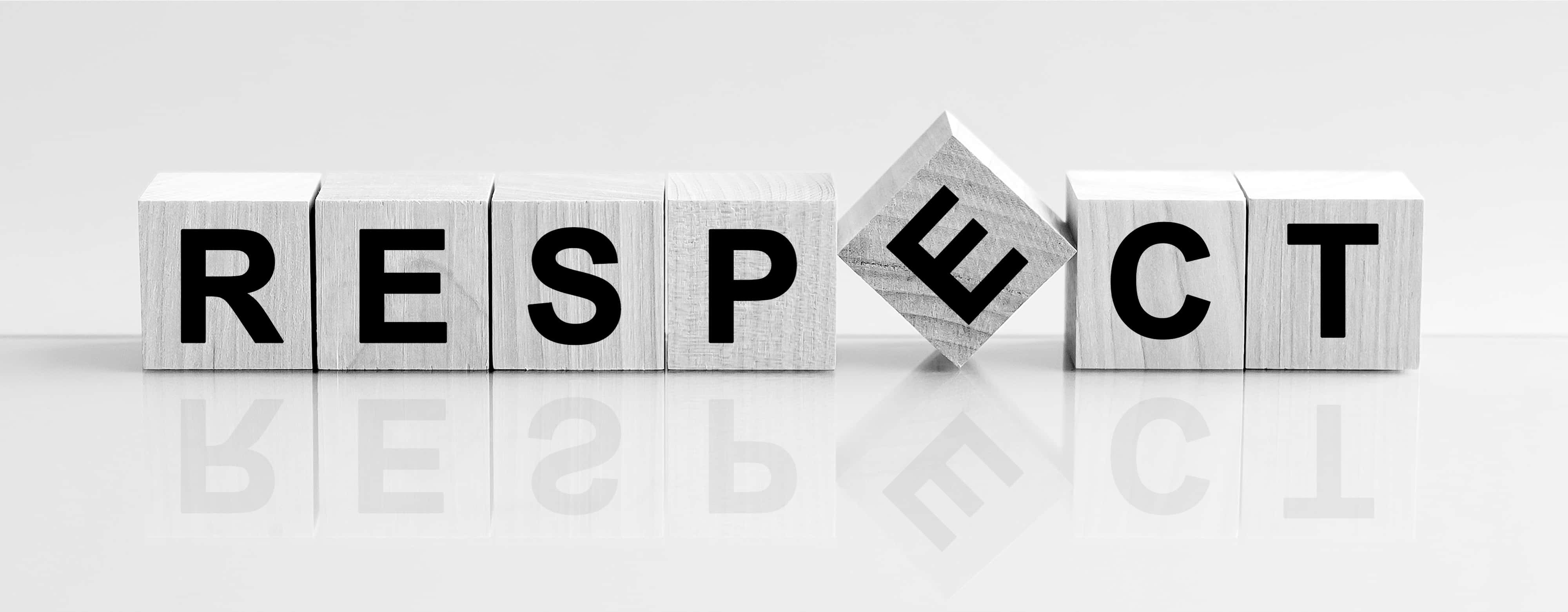 設計 桌布 壁紙 — 木製積木拼出 RESPECT，其中 'E' 傾斜，在光滑的白色表面上投射倒影。