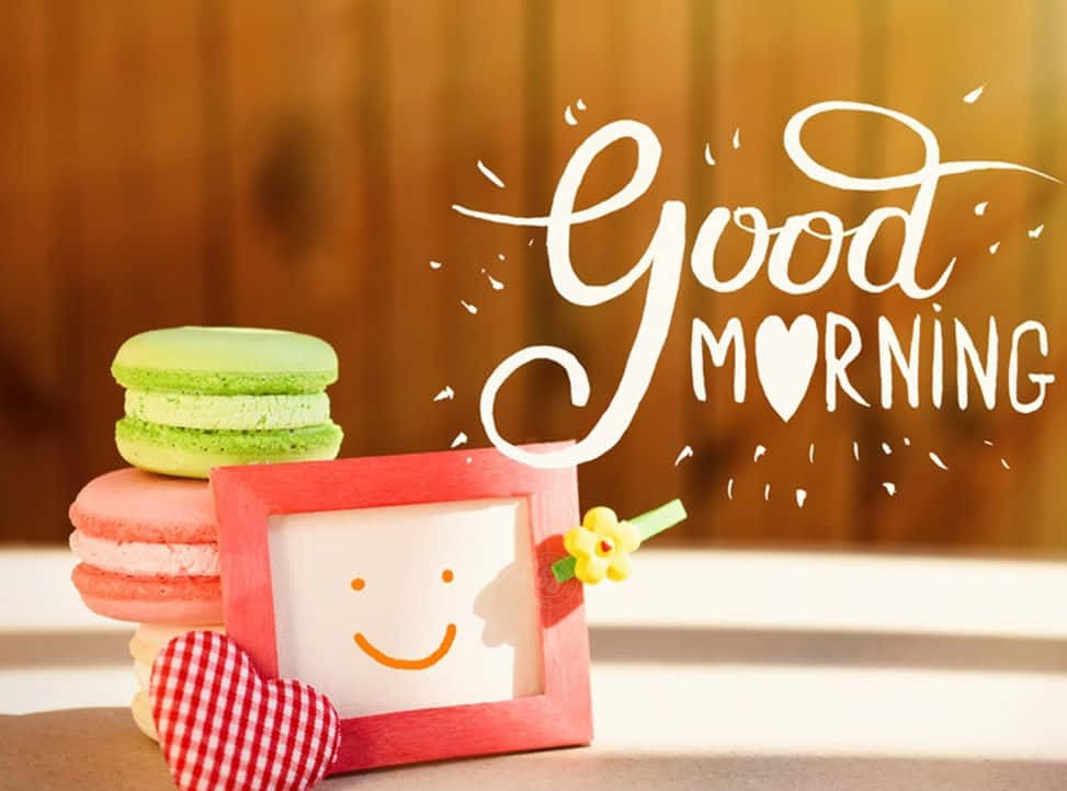 cute good morning 桌布 壁紙 — 木製背景上堆疊的彩色馬卡龍和帶有「早安」文字的笑臉相框。