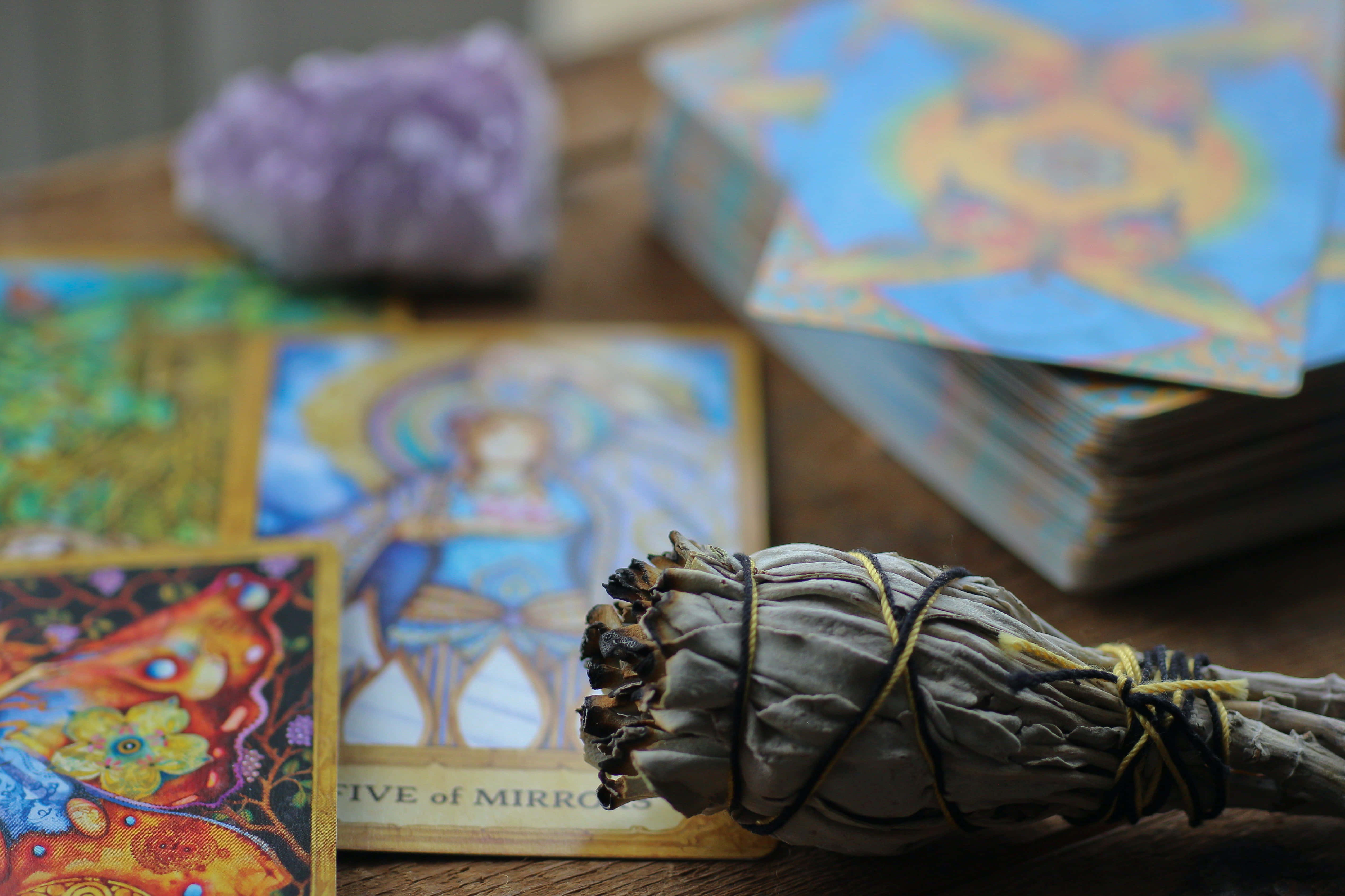 Tarot Card 桌布 壁紙 — 木製表面上，一個煙燻棒放在色彩繽紛的神諭卡和紫色水晶旁邊的特寫。