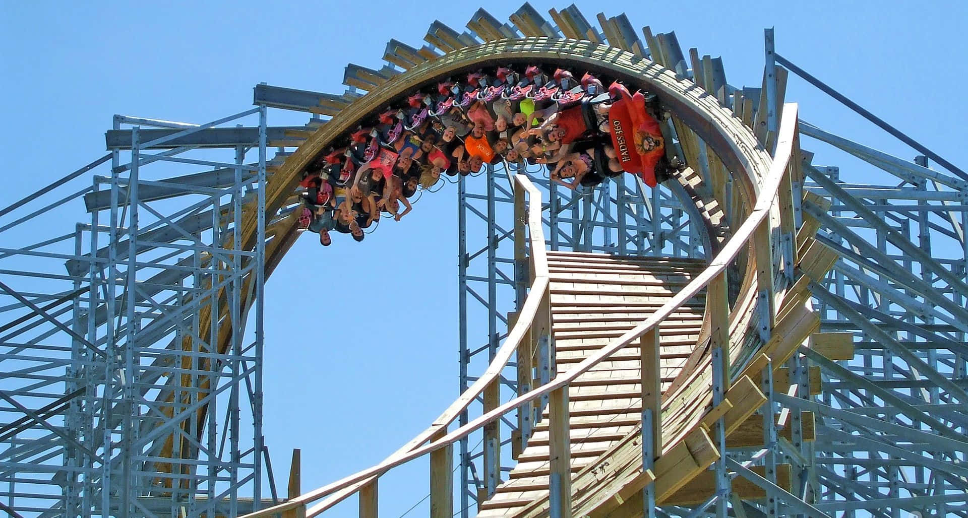 Roller Coaster 桌布 壁紙 — 木製雲霄飛車倒轉迴圈，乘客頭下腳上，襯著清澈藍天。