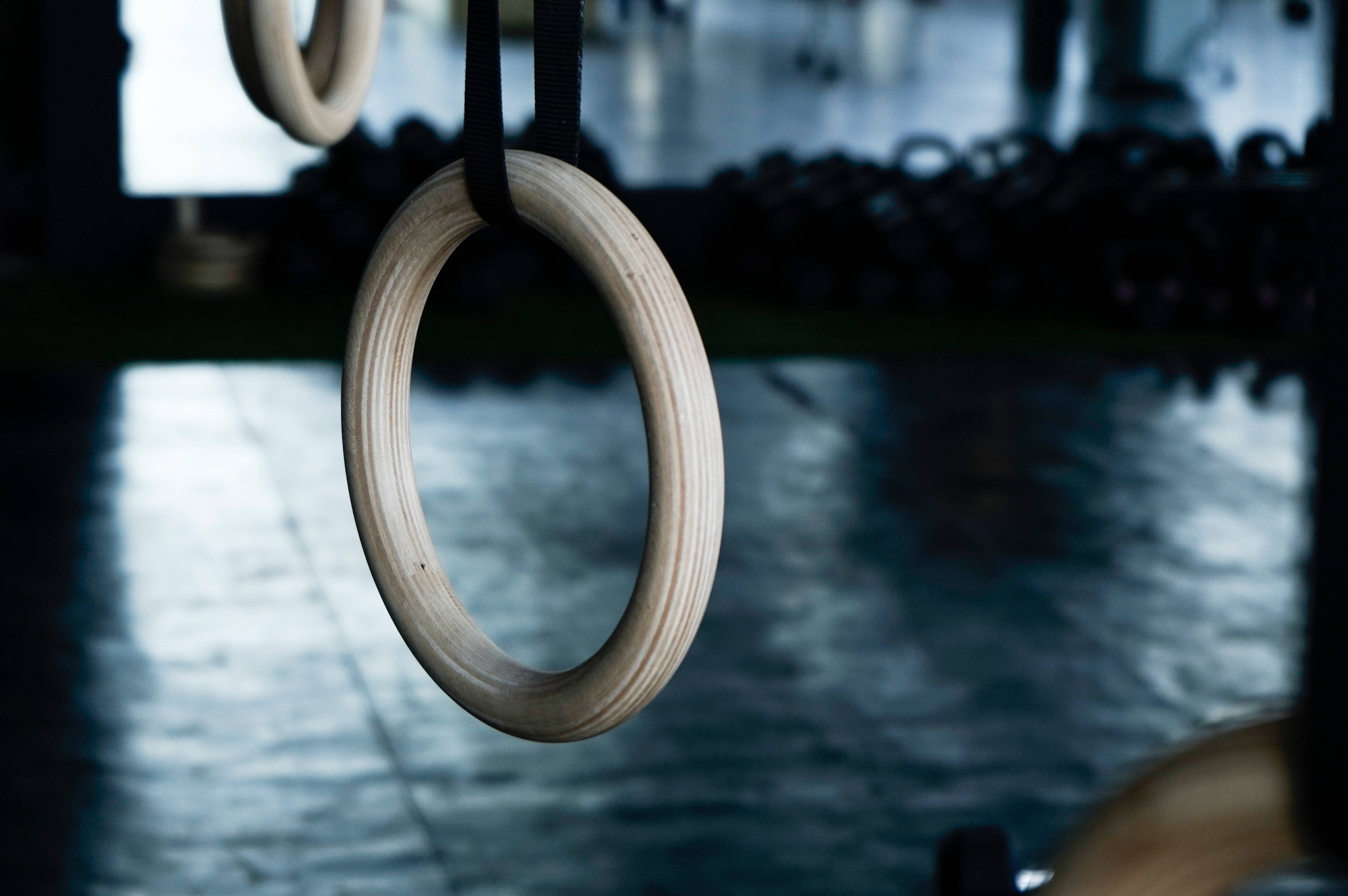 Gymnastics 桌布 壁紙 — 木製體操環掛在昏暗健身房的特寫，背景有模糊的啞鈴。
