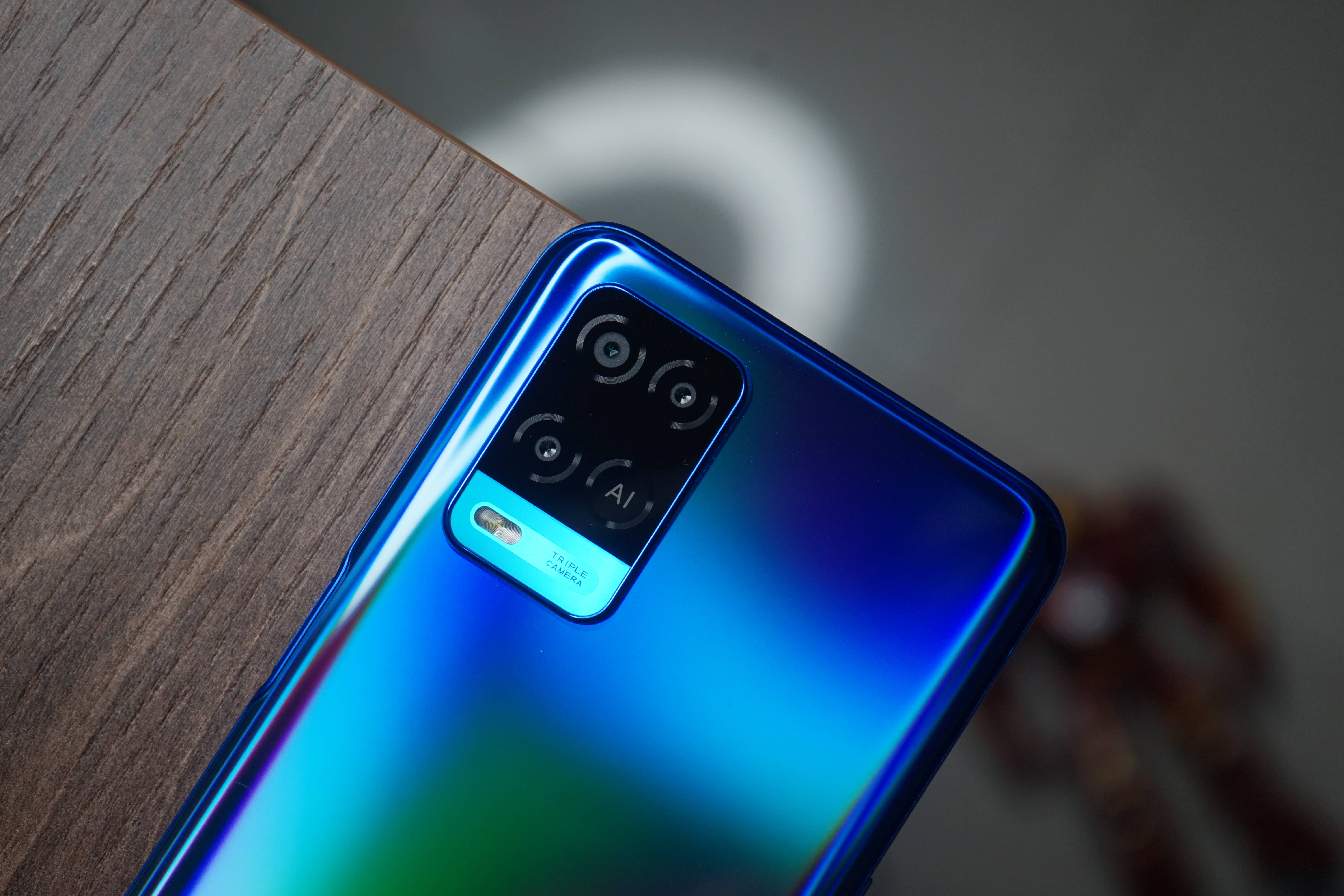 oppo 桌布 壁紙 — 木質表面上放置的藍色漸變智慧型手機特寫，配備三鏡頭設置。
