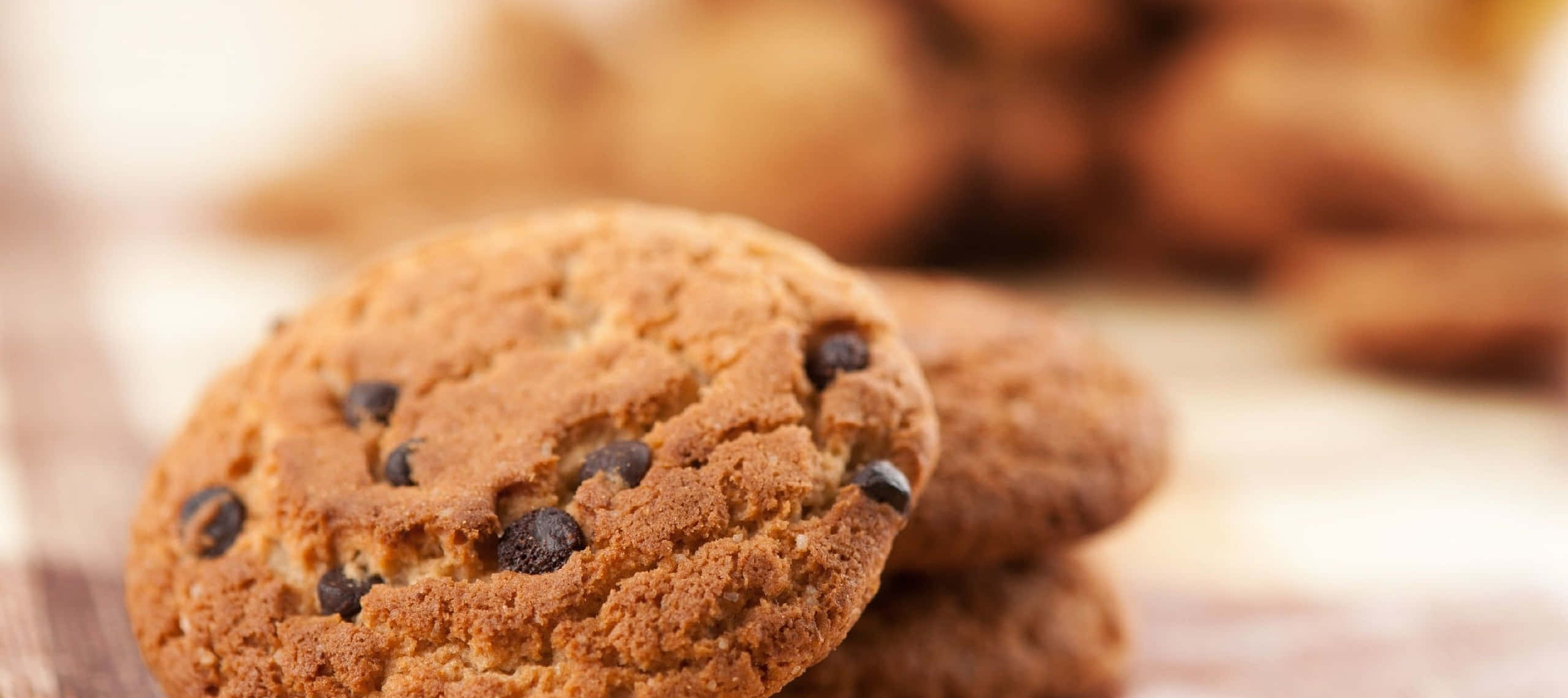 1440p Cookies 桌布 壁紙 — 木質表面上溫暖金黃色巧克力餅乾和融化巧克力碎的特寫。