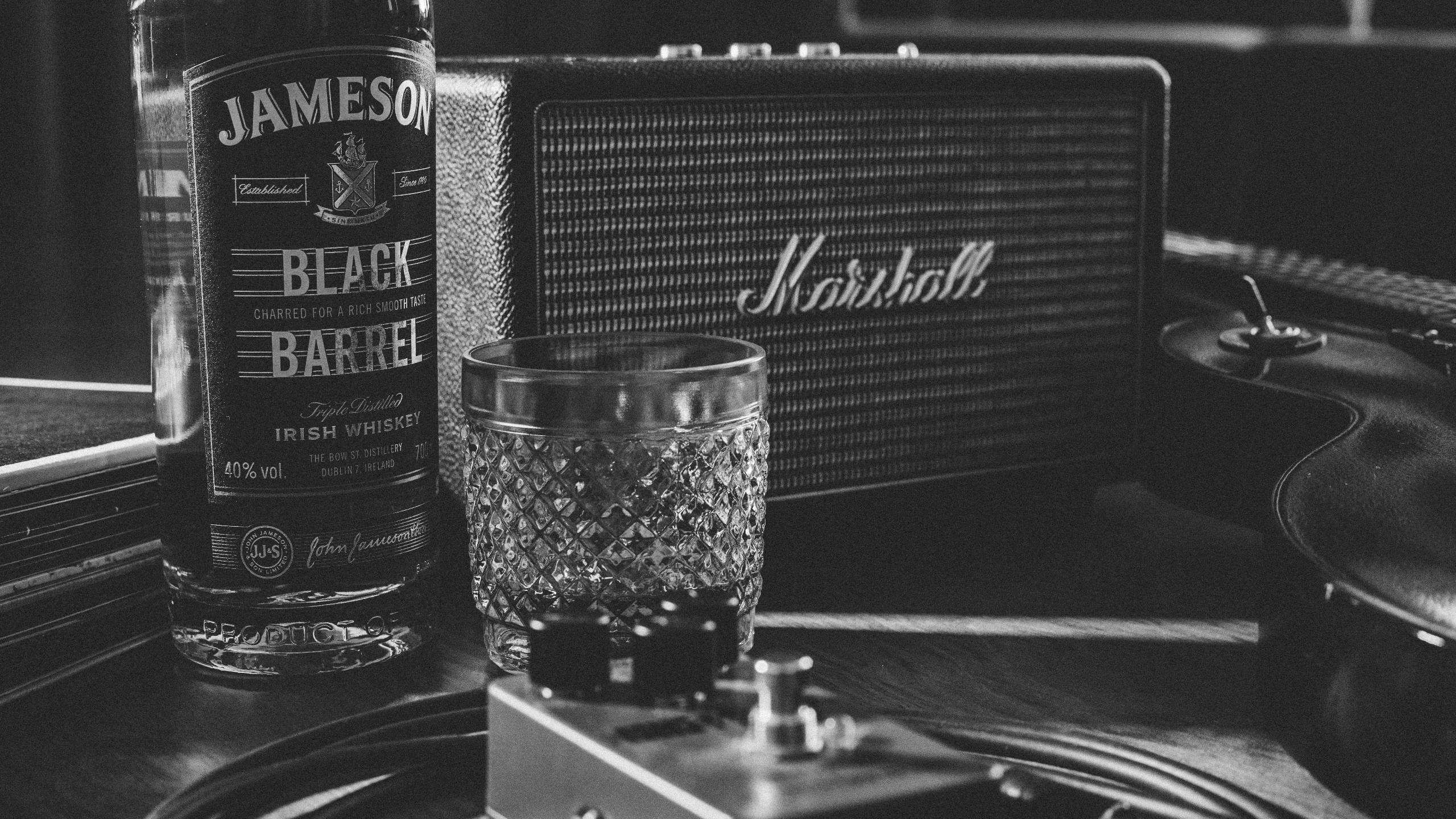 Marshall 桌布 壁紙 — 木質表面上的 Jameson Black Barrel 酒瓶、酒杯和 Marshall 擴音器的單色靜物。