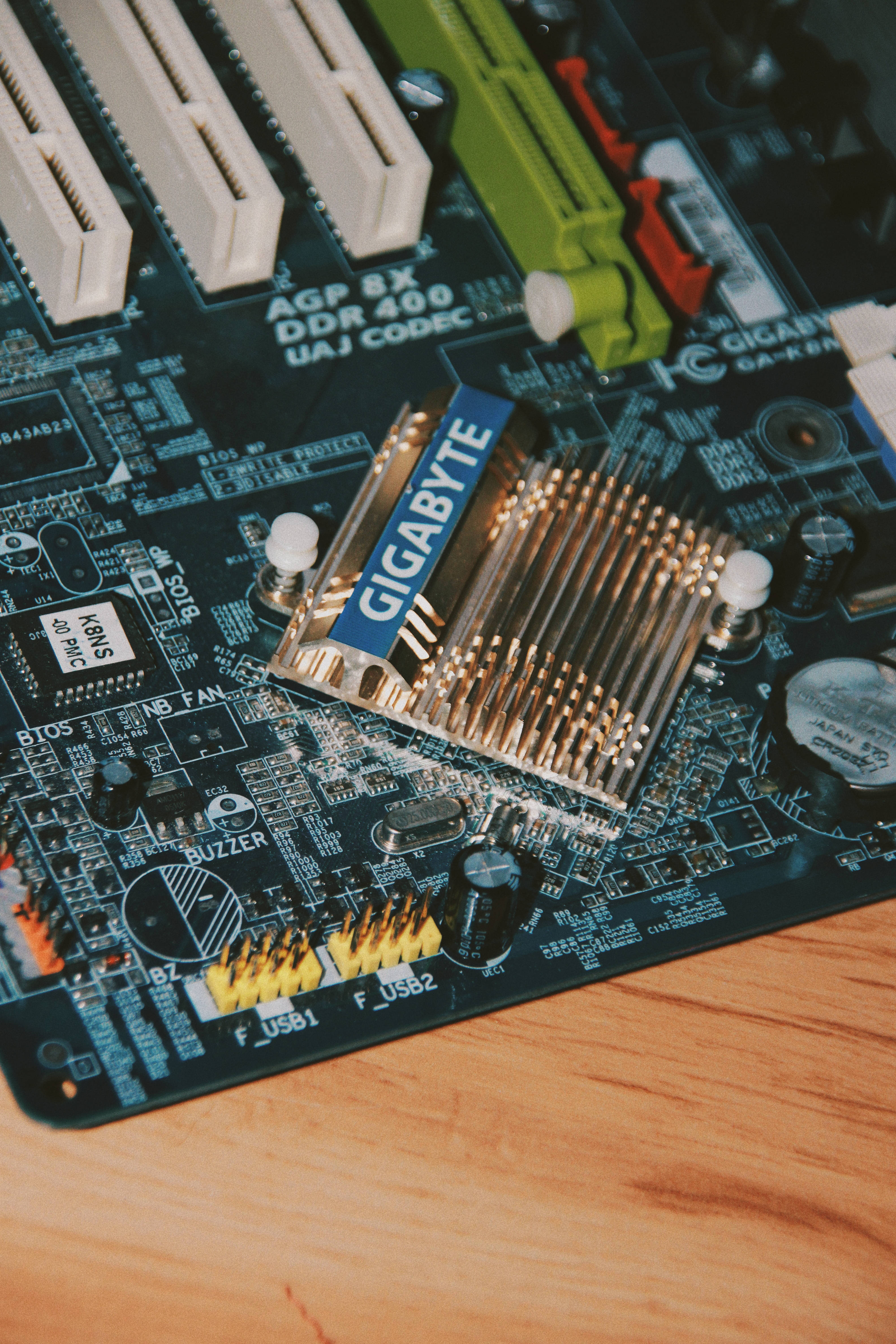 Motherboard 桌布 壁紙 — 木質表面上的Gigabyte主機板特寫，帶有金色RAM插槽和綠色電路。