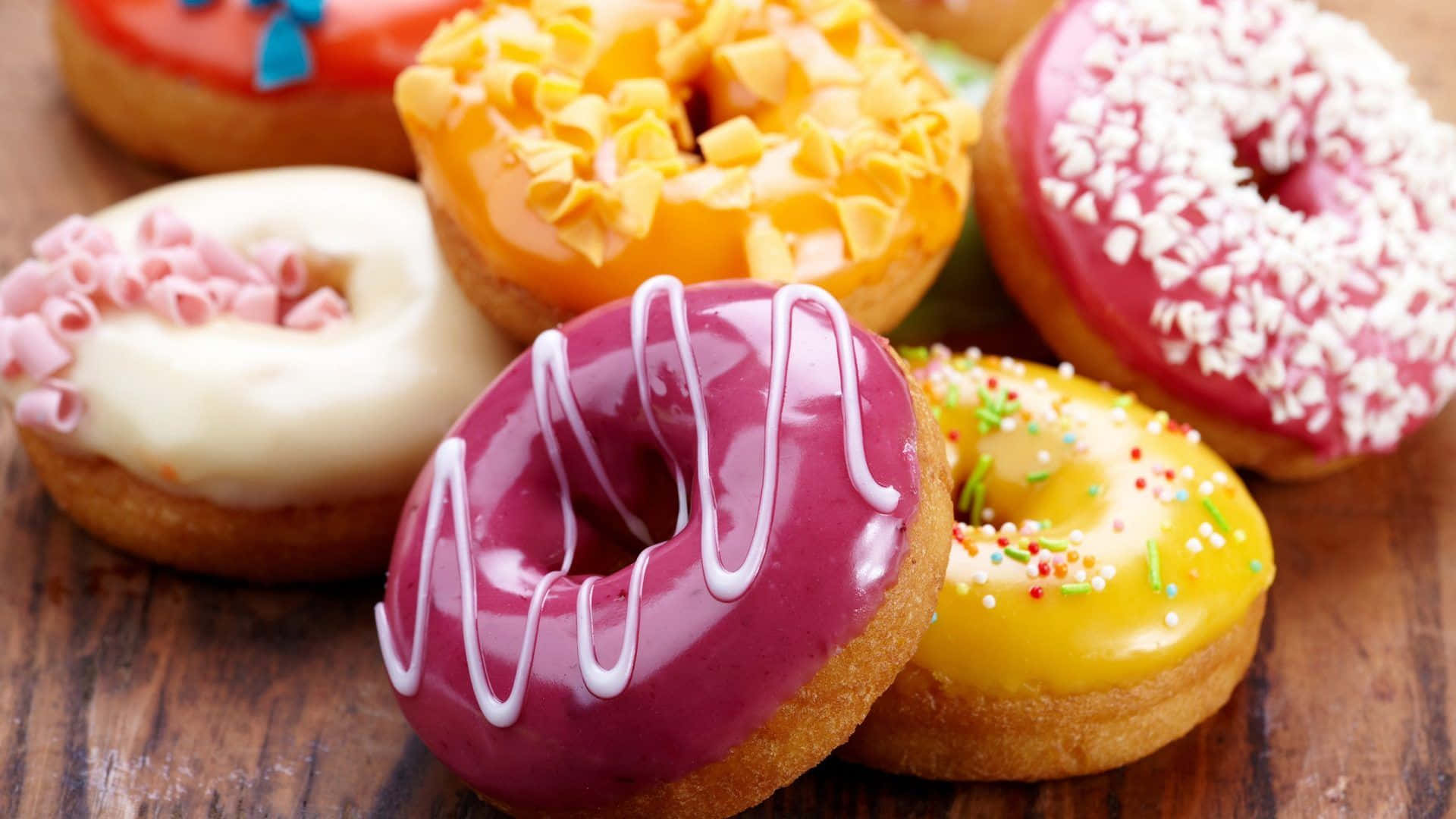 donuts 桌布 壁紙 — 木質表面上色彩繽紛的糖霜甜甜圈，帶有糖粒和糖霜的特寫。