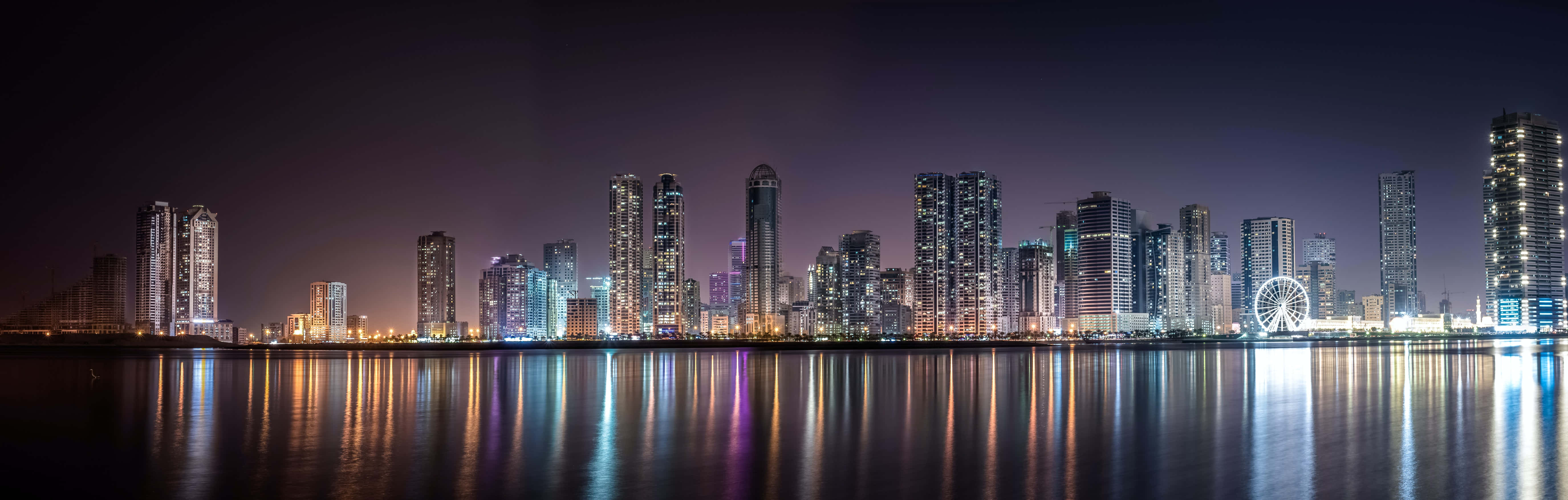 城市風景 桌布 壁紙 — 未來城市天際線的全景夜景，閃爍的摩天大樓倒映在平靜的水面上。
