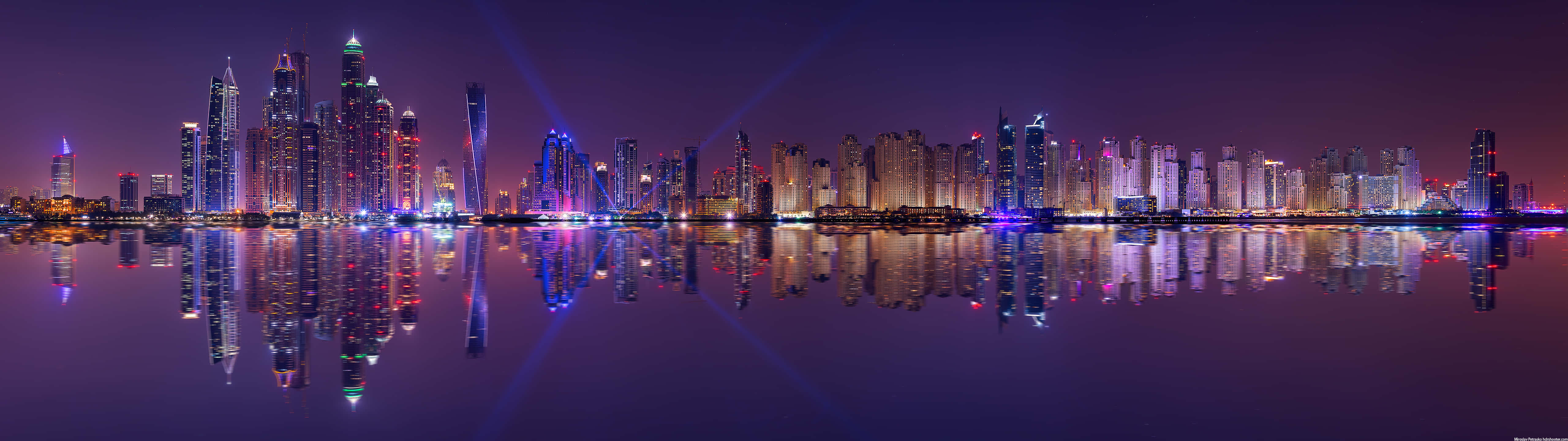 Ultra Wide 桌布 壁紙 — 未來城市天際線的夜景全景，發光的摩天大樓倒映在平靜的水面上。