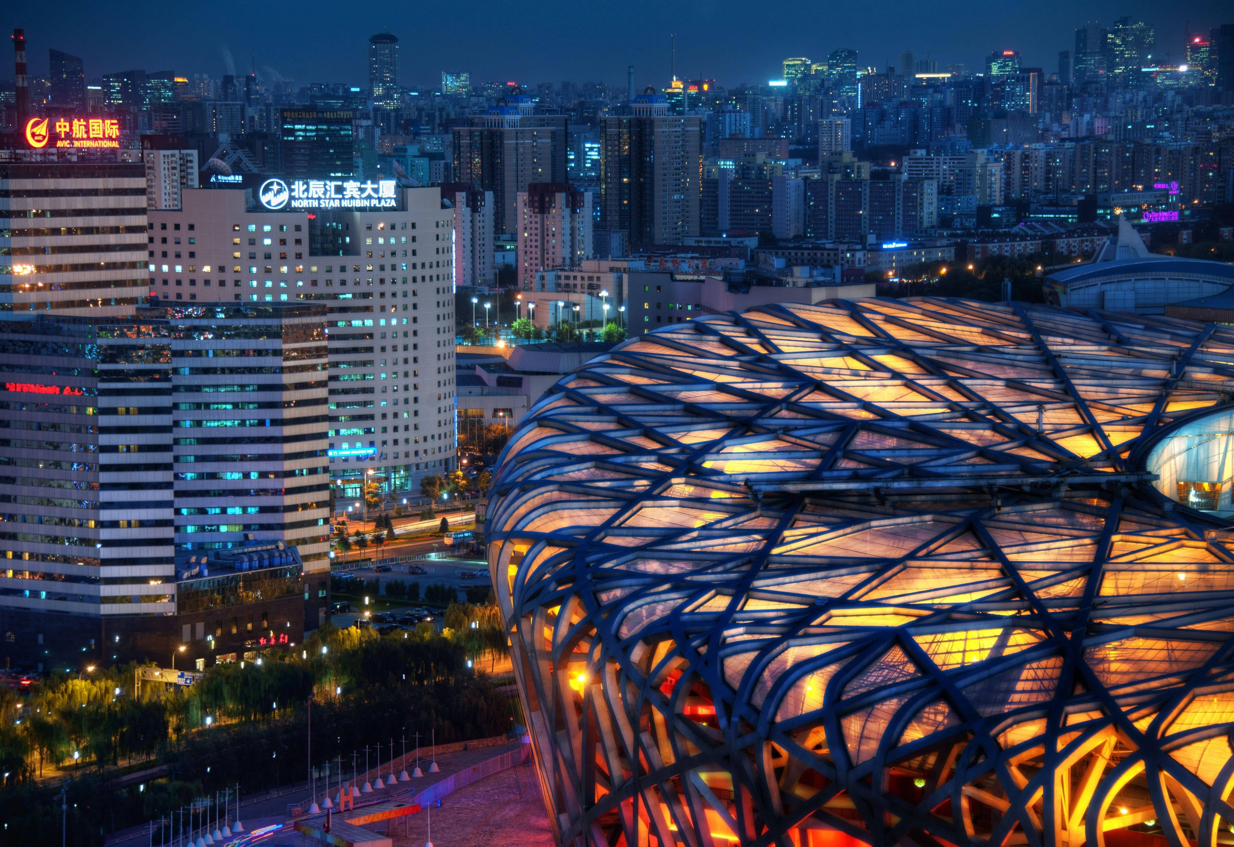 Beijing 桌布 壁紙 — 未來感十足的圓頂建築在燈火通明的摩天大樓背景下溫暖發光的迷人夜景。