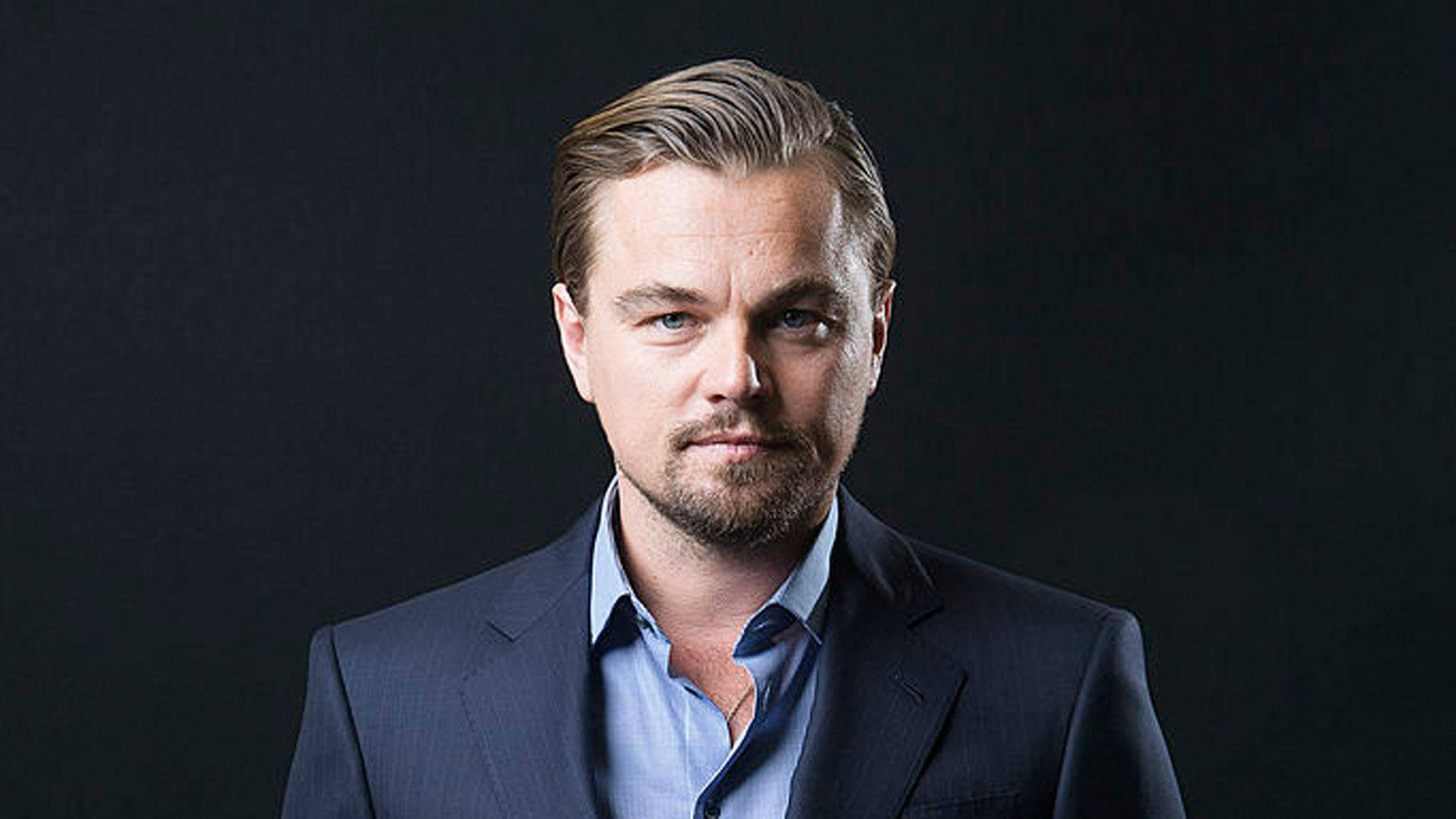 Dicaprio 桌布 壁紙 — 李奧納多·狄卡皮歐在昏暗的攝影棚肖像中穿著海軍藍西裝和淺藍色襯衫，專注地凝視。