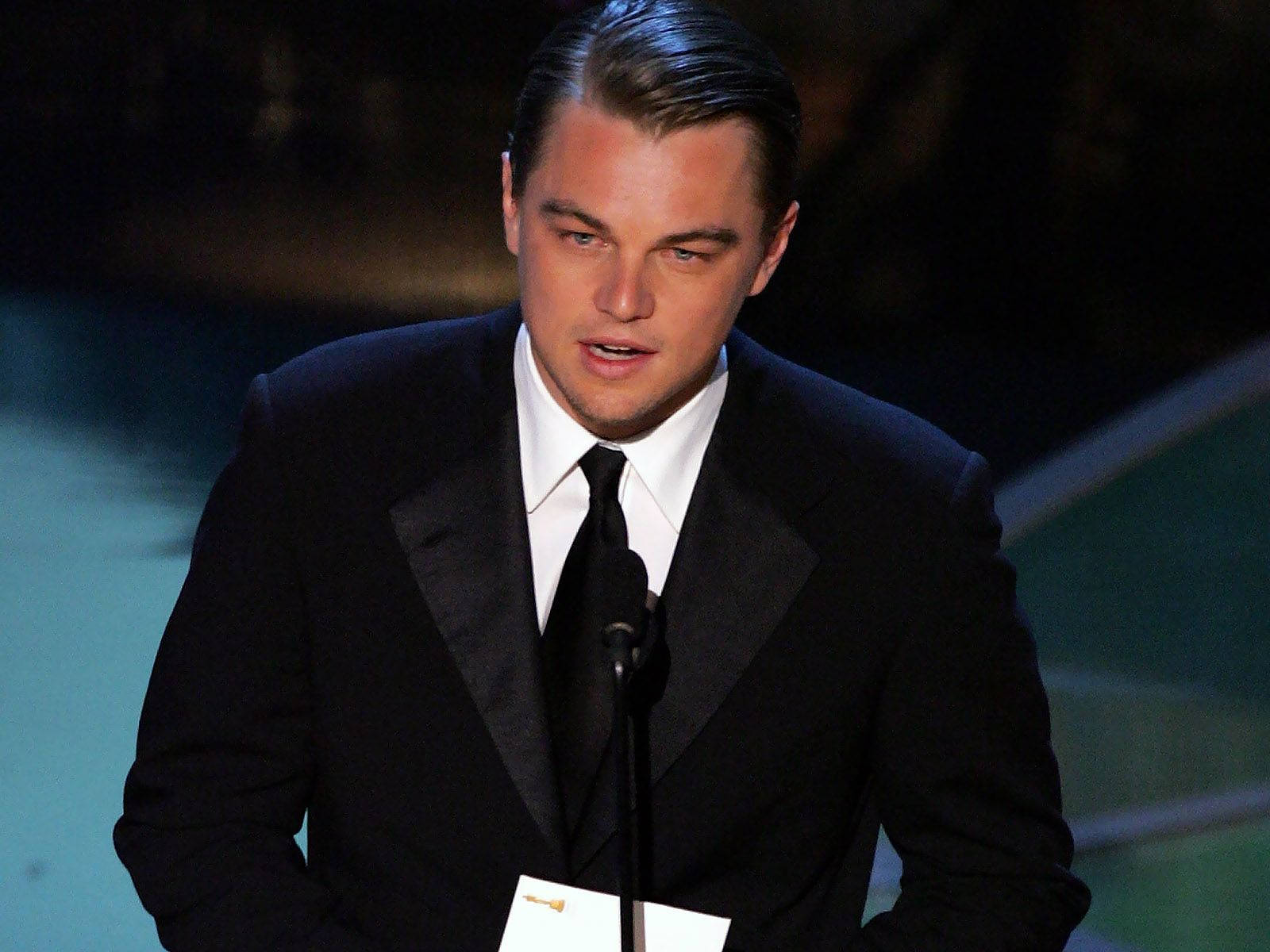 Dicaprio 桌布 壁紙 — 李奧納多·狄卡皮歐在頒獎典禮上穿著黑色燕尾服，在舞台燈光下發言。