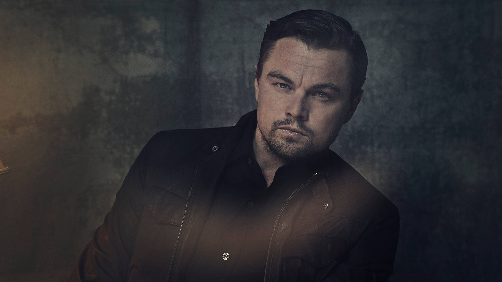 Dicaprio 桌布 壁紙 — 李奧納多·狄卡皮歐穿著深色皮夾克，在質感豐富的陰沉背景下專注凝視。