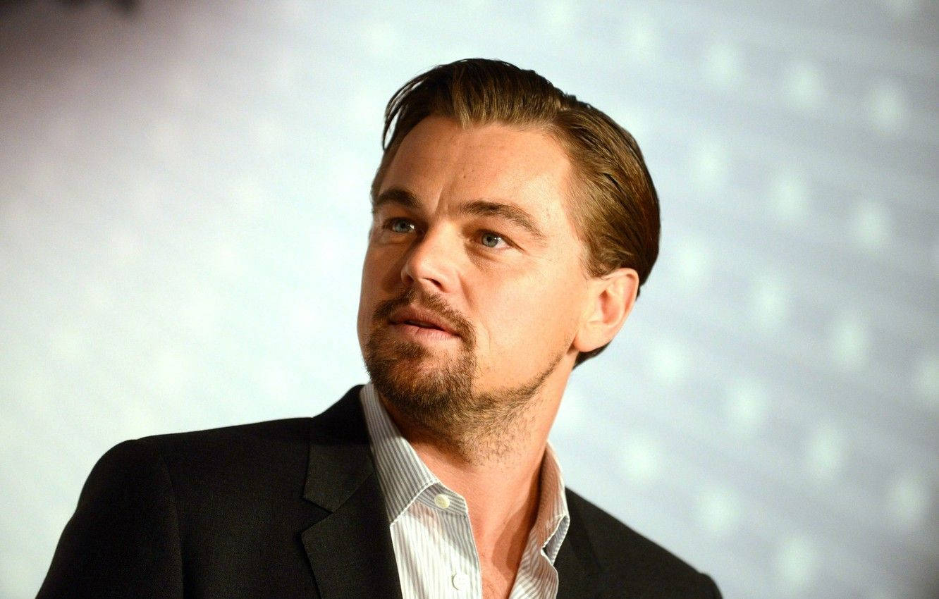 Dicaprio 桌布 壁紙 — 李奧納多·狄卡皮歐身穿深色西裝和條紋襯衫，在柔和燈光和模糊圓形燈光的背景下若有所思地凝視。