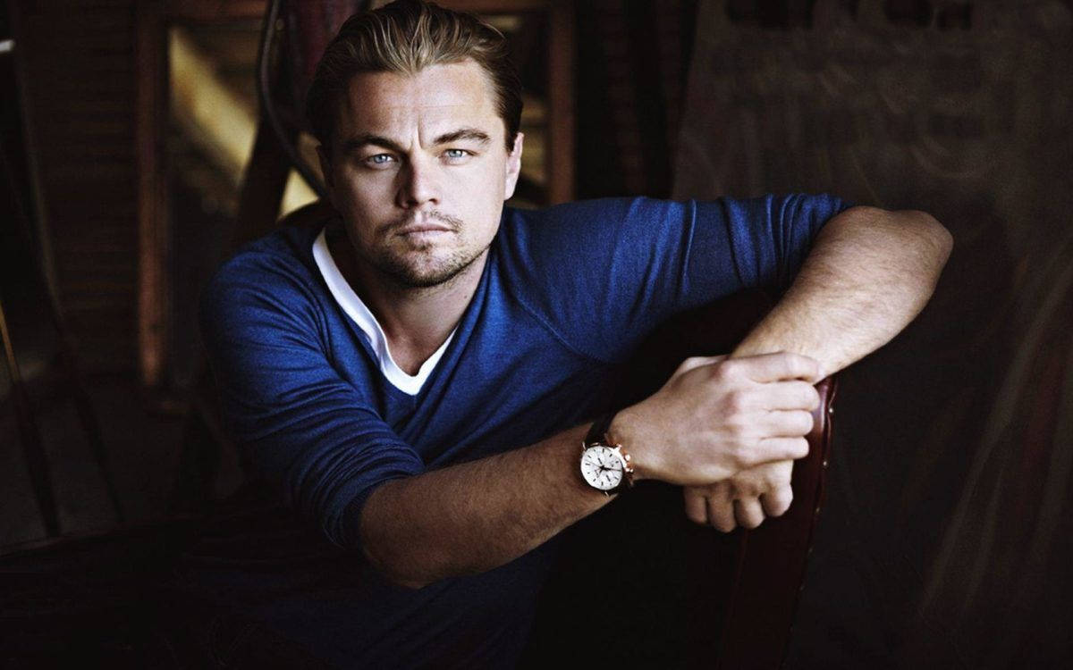 Dicaprio 桌布 壁紙 — 李奧納多·狄卡皮歐身穿藍色毛衣，在溫暖的電影燈光下向前傾，神情嚴肅。