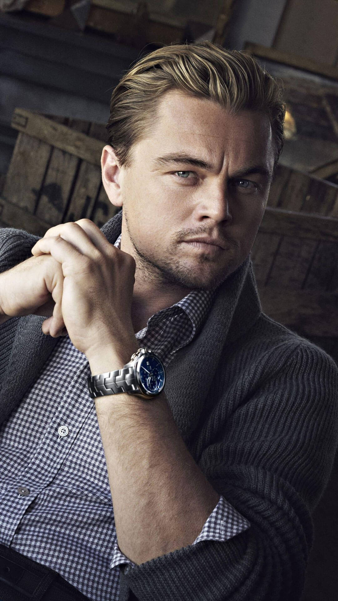 Dicaprio 桌布 壁紙 — 李奧納多·狄卡皮歐雙手緊握，專注地凝視，身穿格紋襯衫和銀色手錶，背景是質樸的木箱。