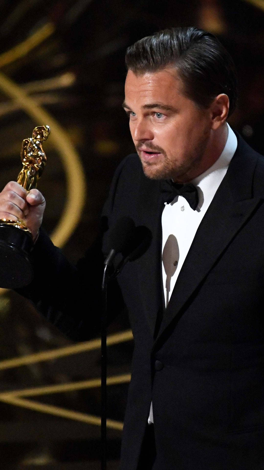 Dicaprio 桌布 壁紙 — 李奧納多狄卡皮歐在頒獎典禮上，在戲劇性的金色燈光下，手持他的金色奧斯卡獎座。