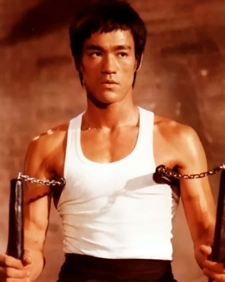 李小龍 桌布 壁紙 — 李小龍在溫暖燈光的簡陋室內環境中，專注地揮舞雙節棍。