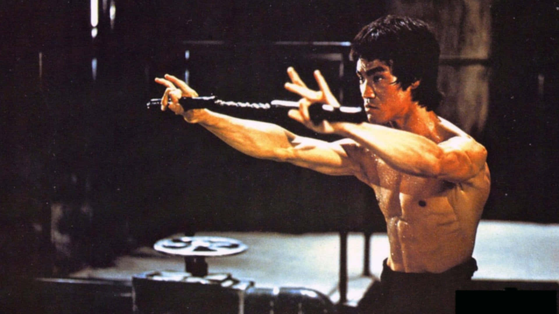 李小龍 桌布 壁紙 — 李小龍在燈光昏暗的健身房中，專注而有力地揮舞雙節棍。