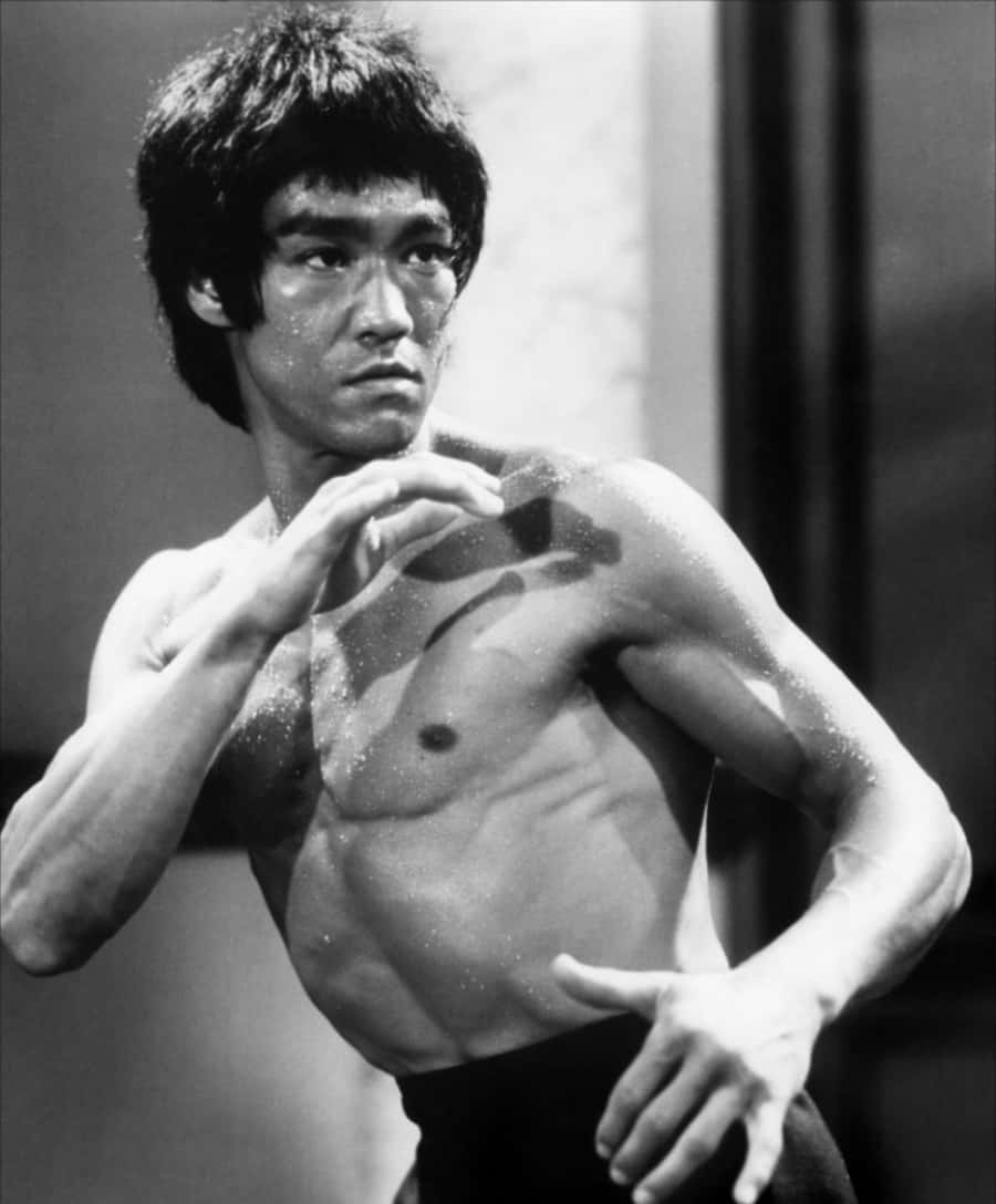 李小龍 桌布 壁紙 — 李小龍專注的武術姿勢，汗水在他肌肉發達的軀幹上閃閃發光，經典黑白照片。