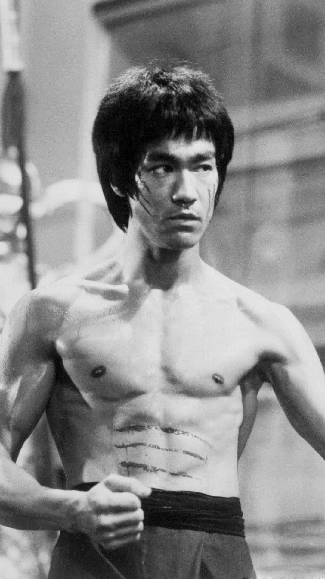 李小龍 桌布 壁紙 — 李小龍赤裸上身，臉上和軀幹帶有戰鬥傷疤，在一張粗糙的黑白照片中凝視著。