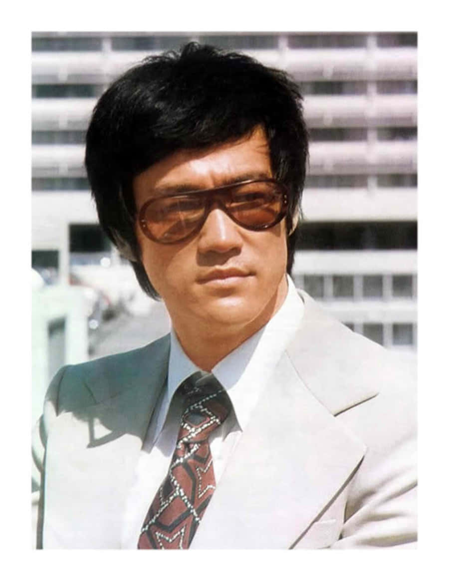 李小龍 桌布 壁紙 — 李小龍身穿淺色西裝及圖案領帶，自信地站在戶外，背後是現代建築。