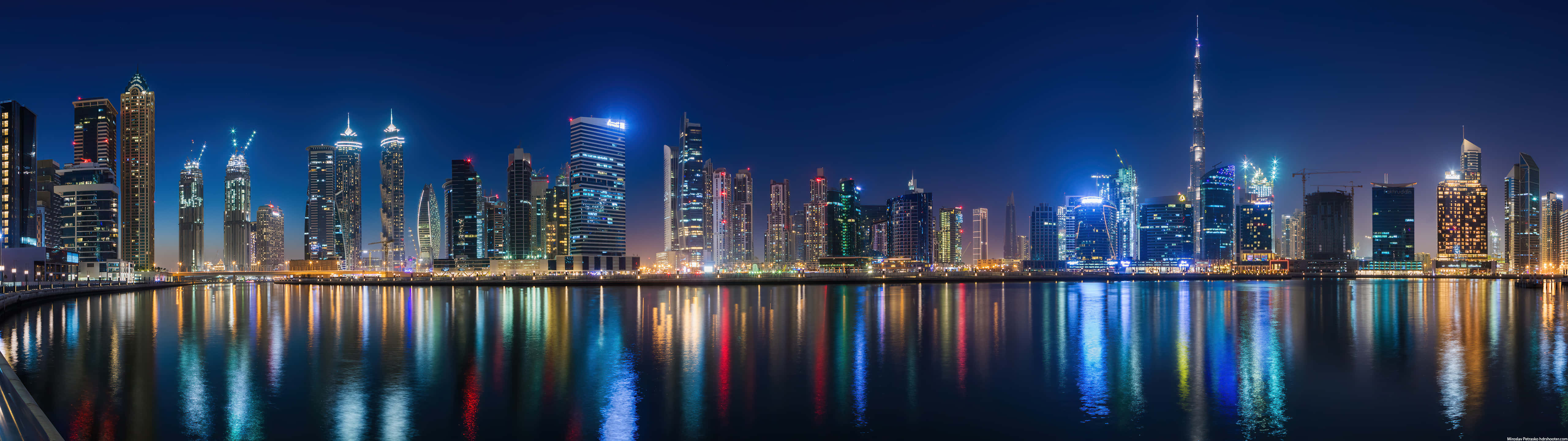 Ultra Wide 桌布 壁紙 — 杜拜令人目眩的夜景，摩天大樓在漆黑的天空中閃耀，燈光完美地倒映在平靜的水面上。