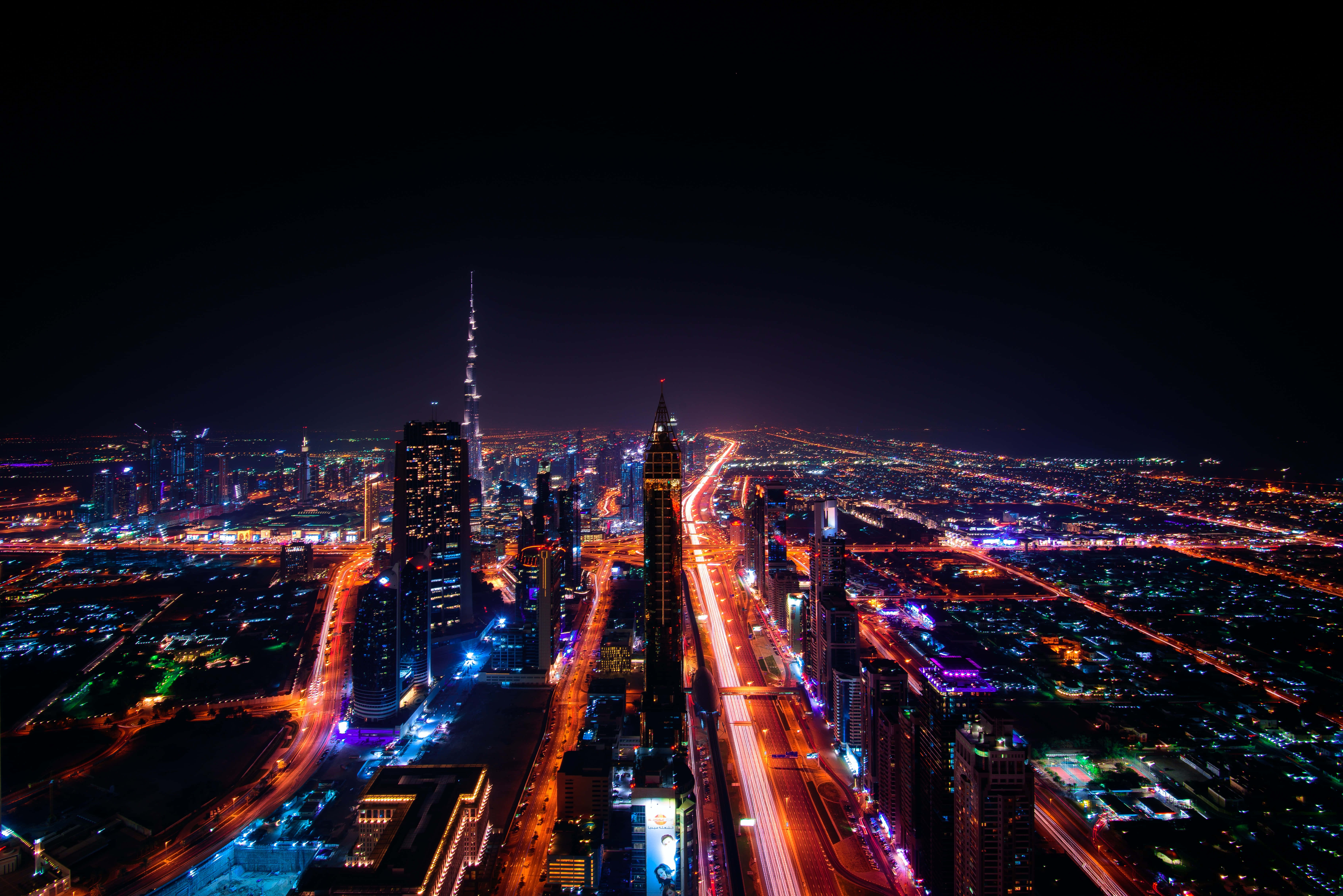 夜景城市 桌布 壁紙 — 杜拜天際線的夜間空拍，哈里發塔閃耀，交通燈光軌跡照亮城市景觀。