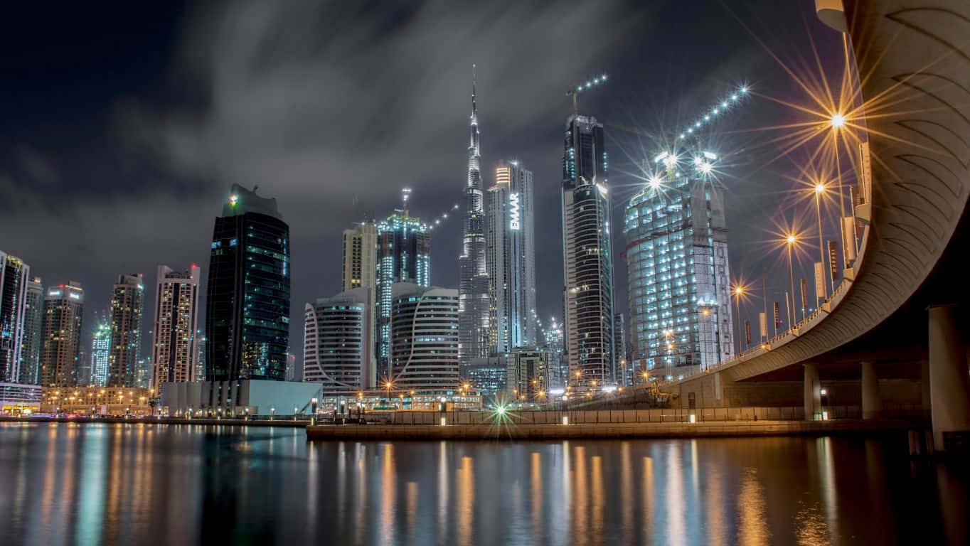1364x768 桌布 壁紙 — 杜拜天際線的璀璨夜景，哈里發塔聳立在發光的摩天大樓之上，倒映在弧形橋下的平靜水面上。